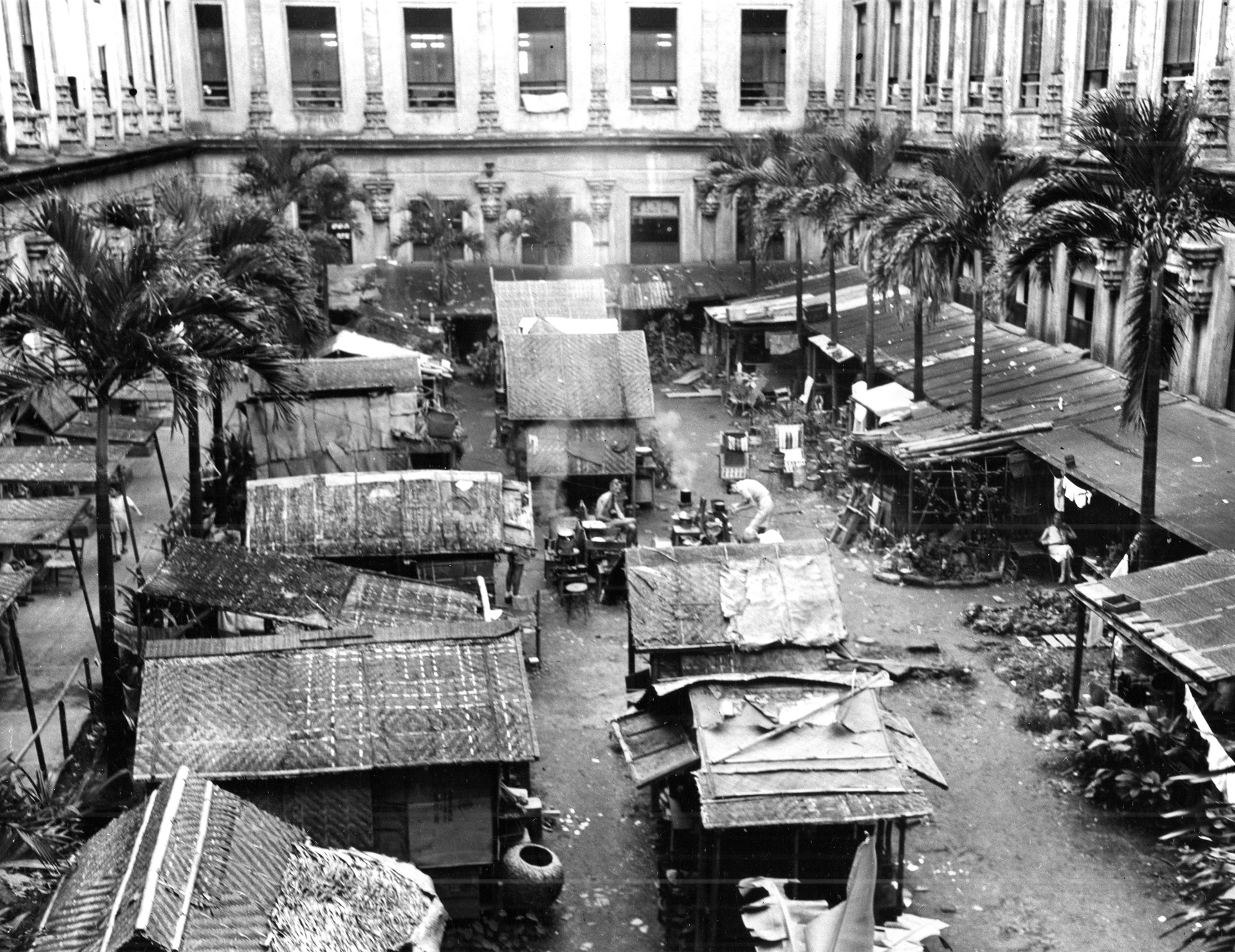 A once beautiful courtyard on the grounds of Santo Tomas University has been turned into a dismal cluster of residential shacks by internees who suffered nearly three years of privations under Japanese rule. 
