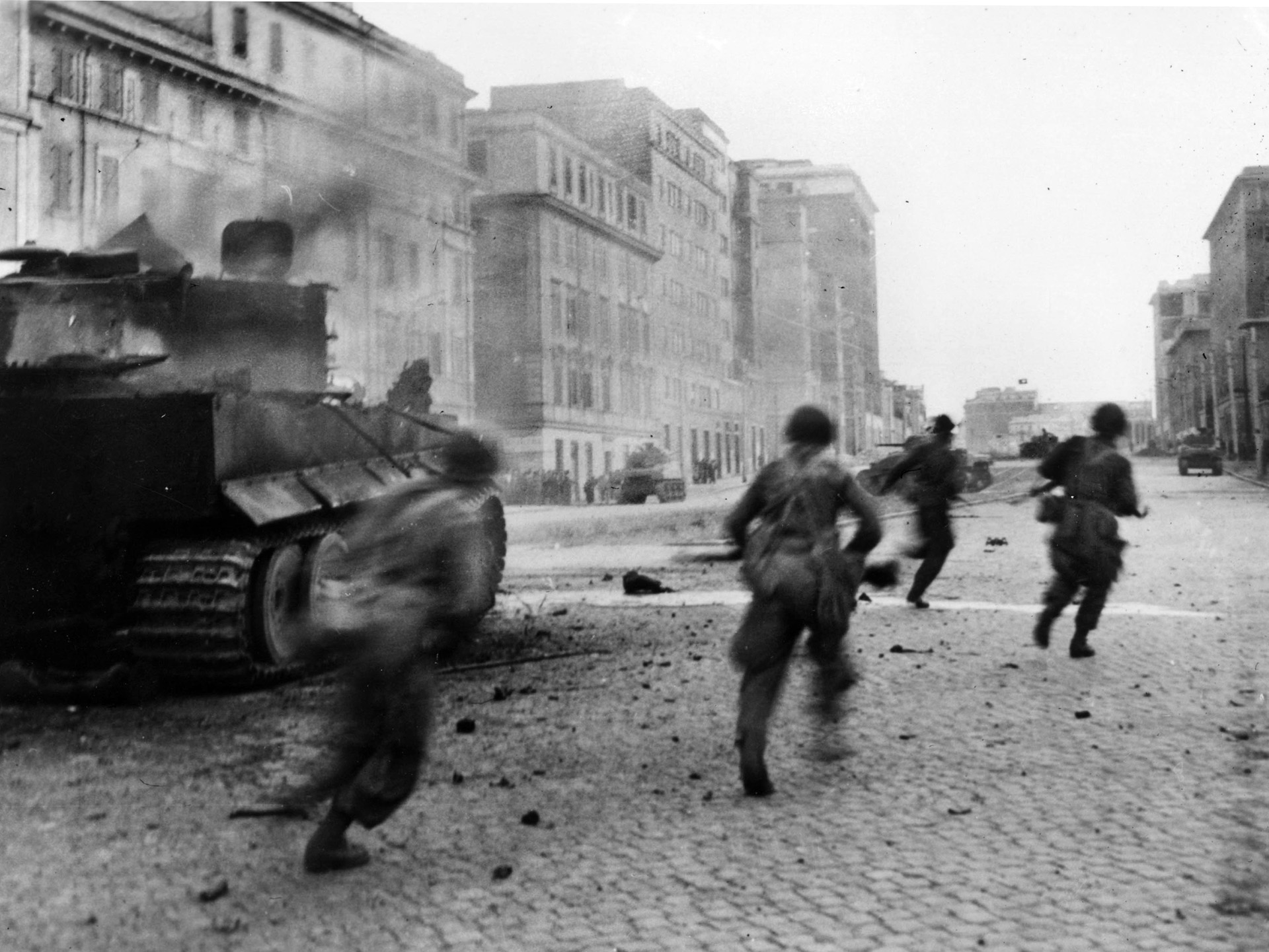 By early June 1944, American troops were fighting on the outskirts of the Eternal City. In this photo American soldiers rush past the smoking hulk of a knocked-out German tank sitting on a street in the Italian capital. By then Kesserling had moved his forces north again.