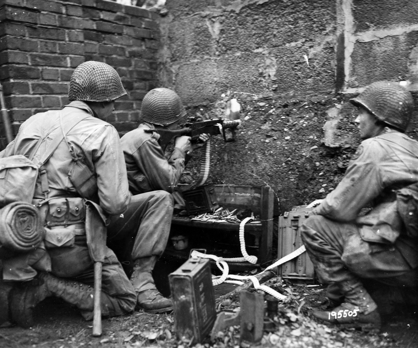 In this photo, taken in the midst of a firefight in Kohlshed, Germany, 3rd Division soldiers fire a machine gun through a hole in a wall at enemy soldiers hidden in a barn 300 yards away.