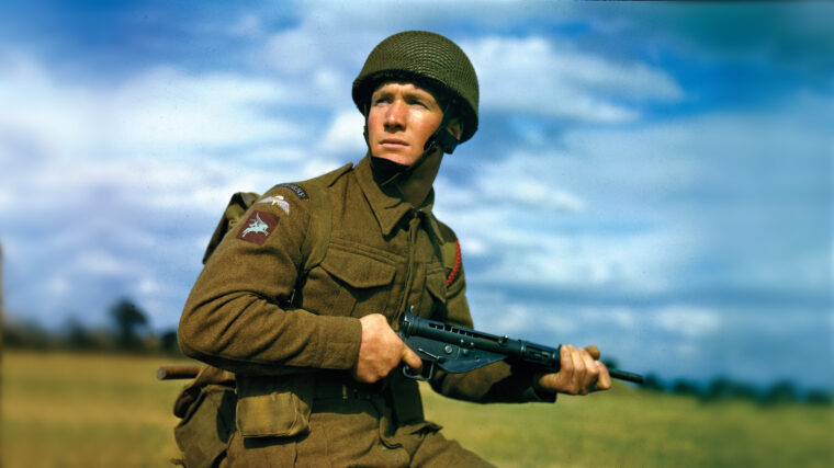 A British airborne soldier, identifiable by his sleeve patch showing Bellerophon riding the flying horse Pegasus, poses for a publicity photo with his Sten gun. To assault the Merville Battery, airborne troops landed both by glider and parachute, but the attack began unraveling from the beginning.