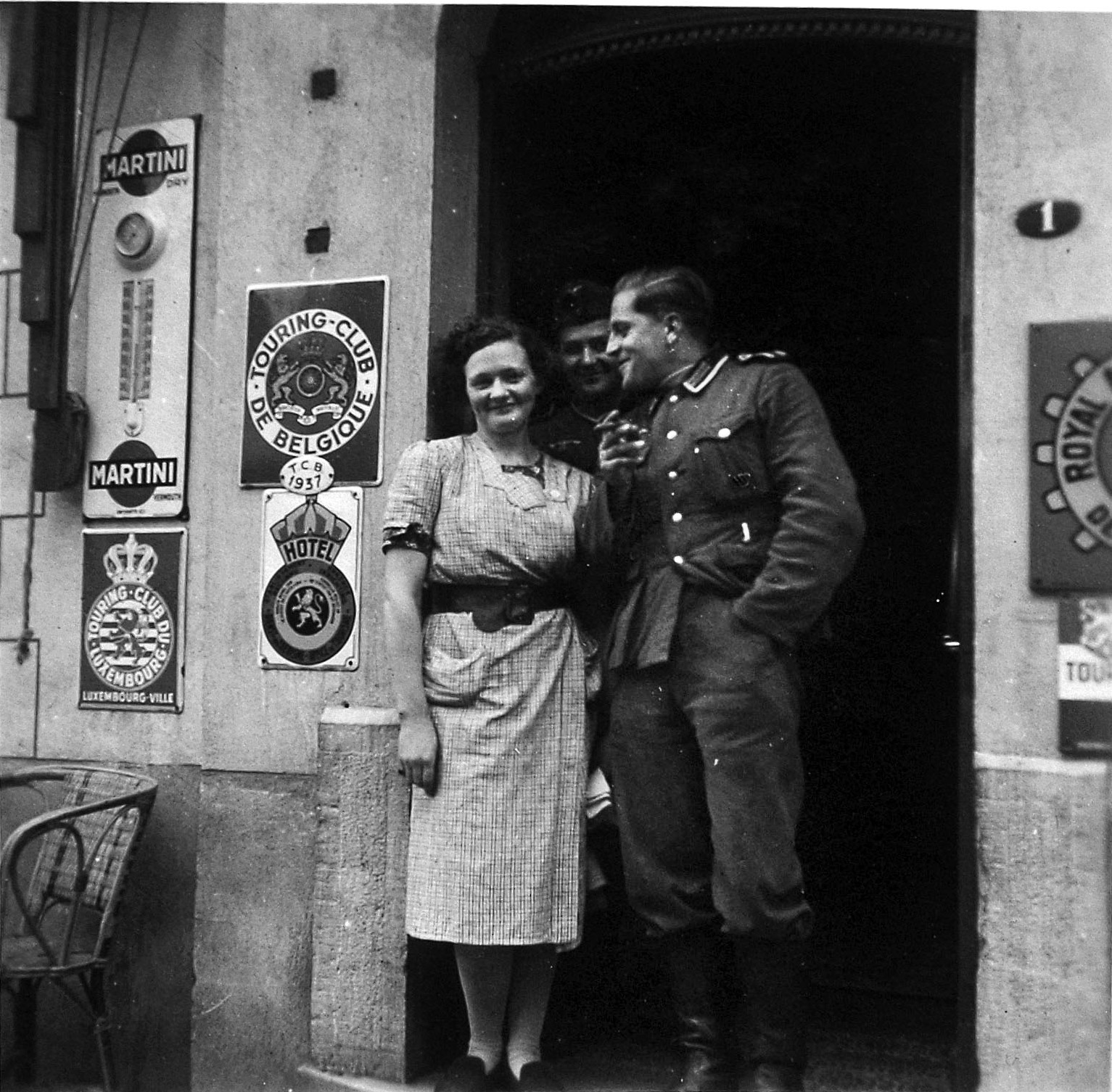 After the 1940 invasion of Belgium, attentive German soldiers make the acquaintance of a Belgian woman in the doorway of a hotel on whose walls are posted the signs of various tourist and automobile organizations. Fraternizing with the local female population was naturally a major point of interest for young German men in uniform; however, the postwar repercussions for “collaborationist” women were often very harsh.