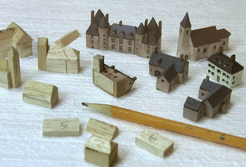 The author made the buildings using balsa wood. He attached the buildings to the board using double-stick carpet tape.