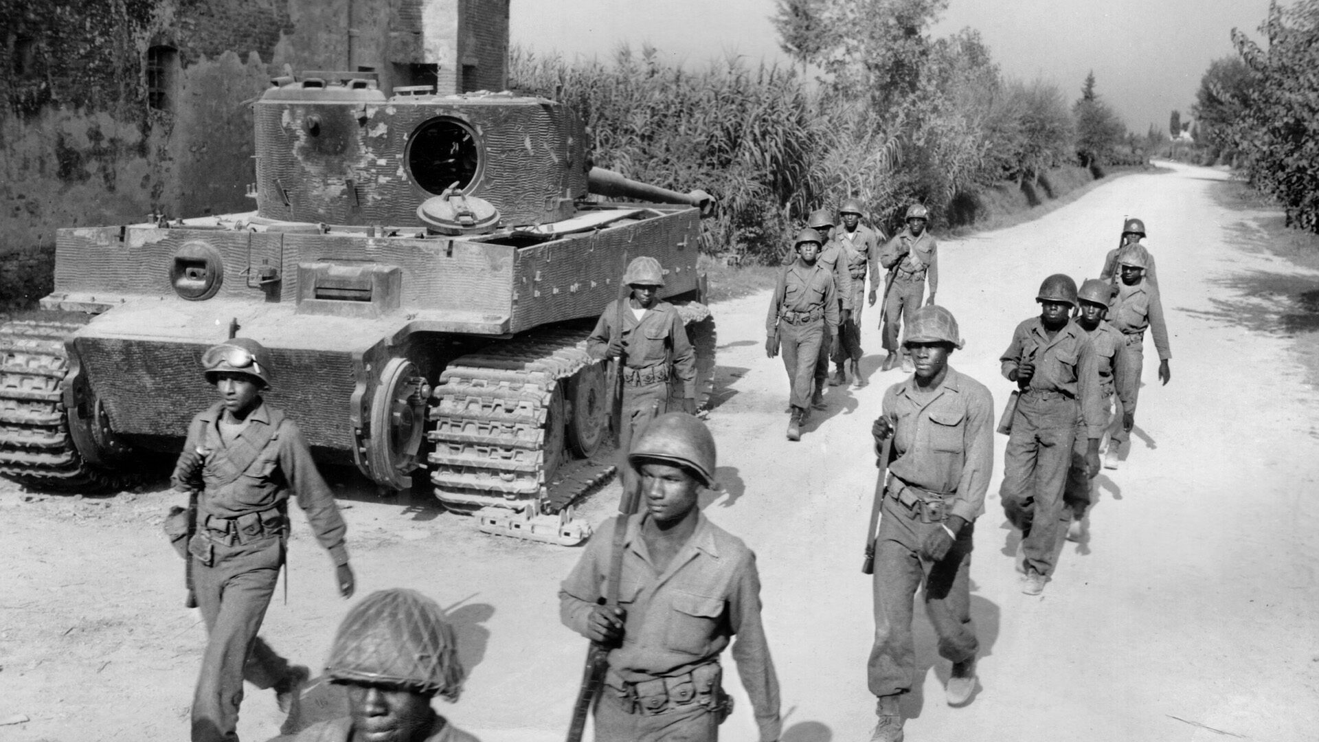 Fighting men of the 92nd Infantry Division, the famed Buffalo Soldiers, march past the wreckage of a knocked out PzKpfw. VI Tiger tank in the vicinity of Ponsacco, Italy. The African-American soldiers of the 92nd Division fought racial injustice in their own army, as well as the Germans.