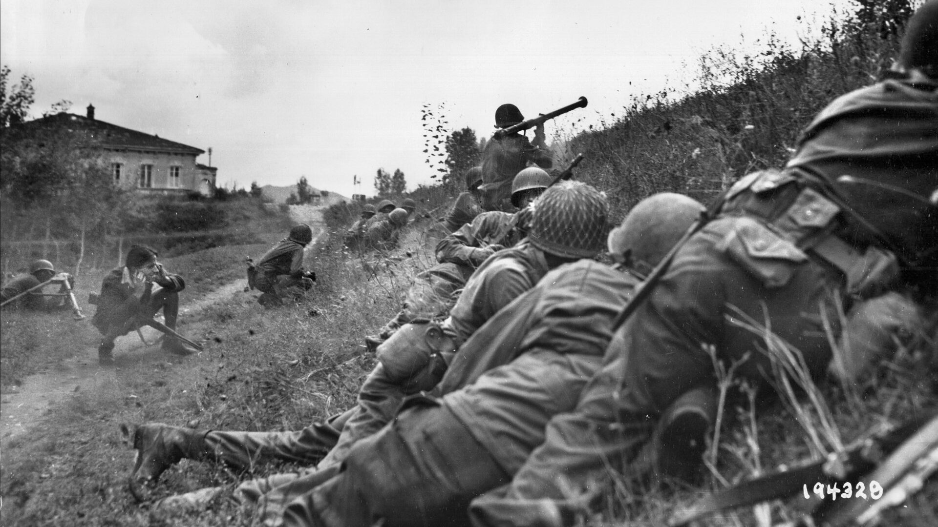 Soldiers of the 92nd Infantry Division engage the Germans on September 7, 1944, three miles north of the town of Lucca, Italy. A soldier rises up to fire a bazooka at a German machine-gun nest just 30 yards from the American position, while an Italian partisan at left covers his ears.
