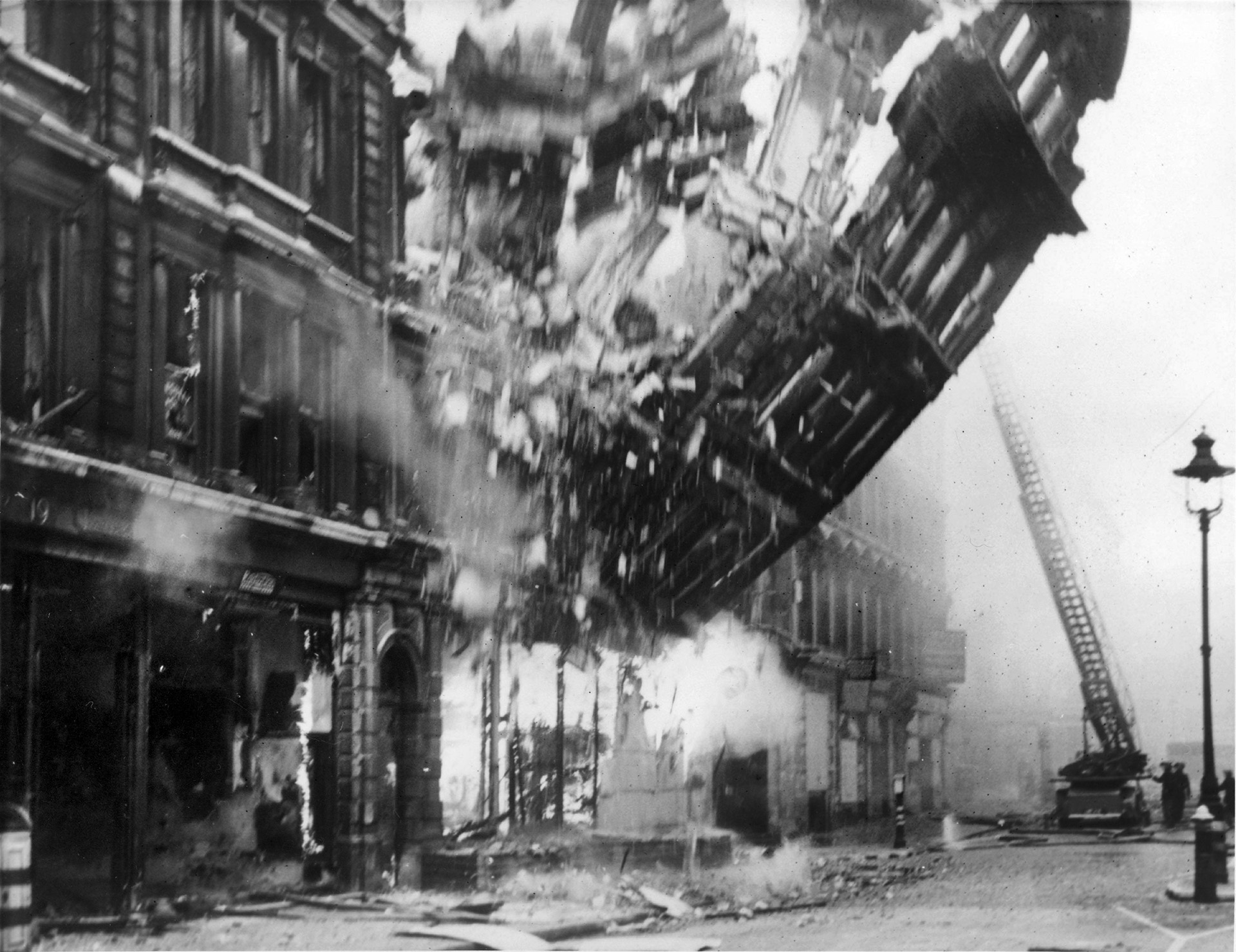 The façade of another building on Queen Victoria Street is captured in mid-collapse in this startling image. German incendiary bombs had burned the heart out of the structure, and weakened it so that the exterior toppled in spectacular fashion while firefighters watched from nearby.