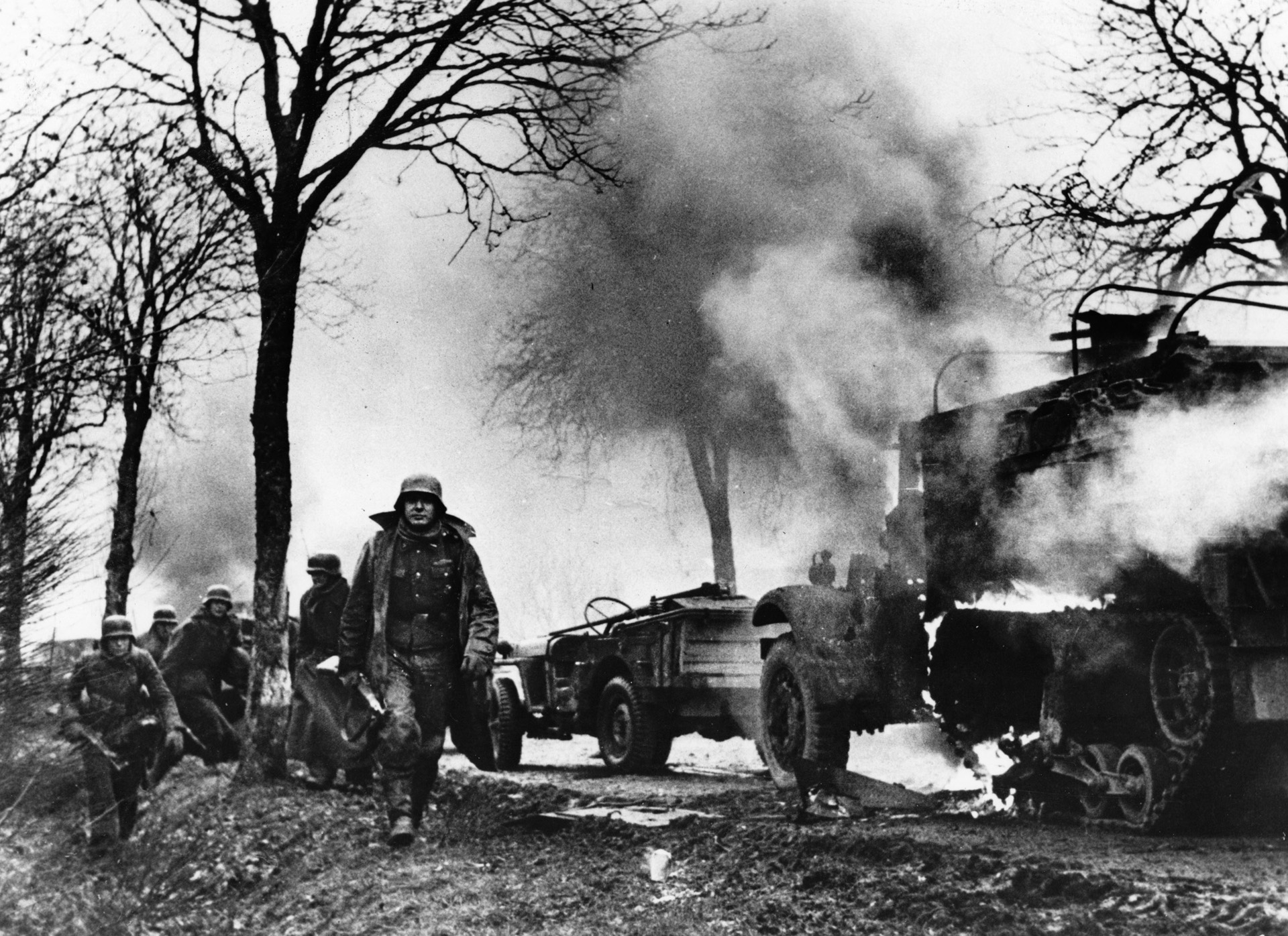 German soldiers of Kampfgruppe Hansen, one of them carrying an assault rifle, advance past burning vehicles of the U.S. 14th Mechanized Cavalry Group. The American column had been overwhelmed minutes before this photo was taken, and the image is from four rolls of film captured from a German soldier during subsequent fighting.