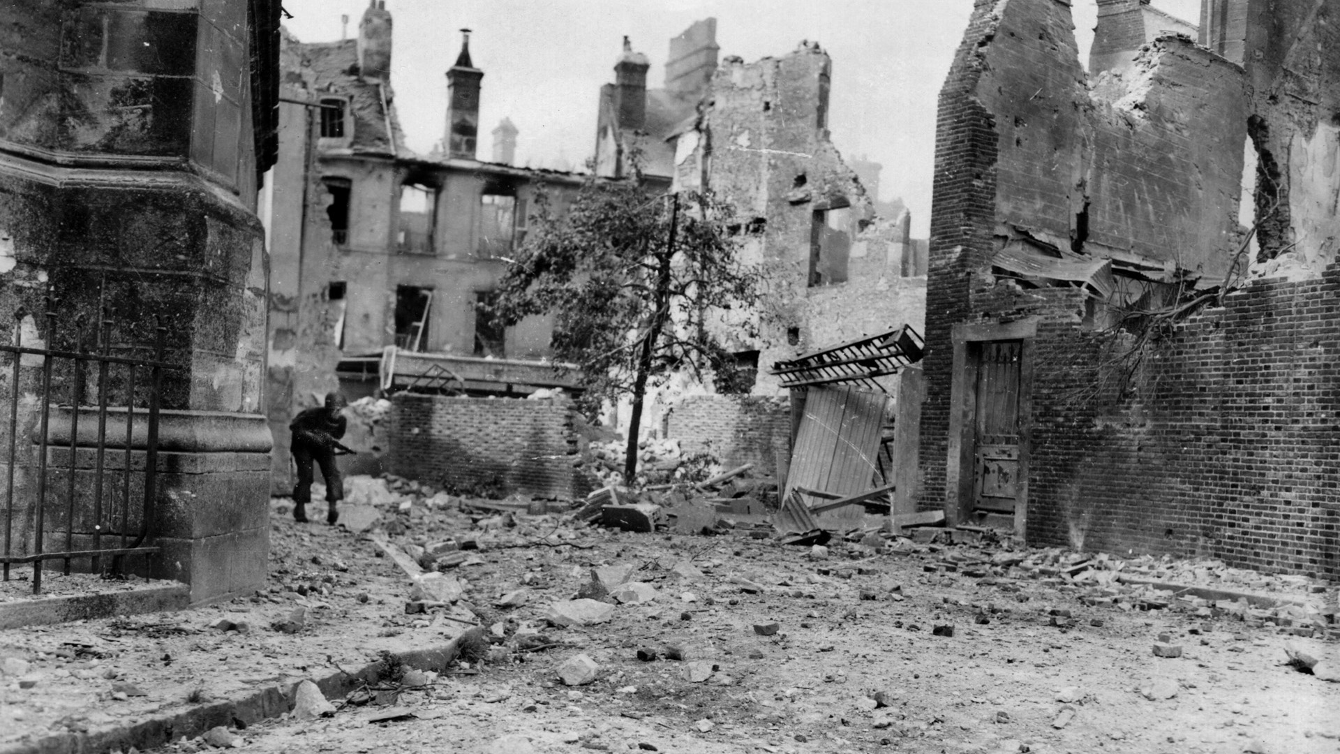Armed with a Thompson submachine gun, an American soldier of the 80th Division proceeds warily through a rubble strewn street in Argentan searching for remaining Germans. 