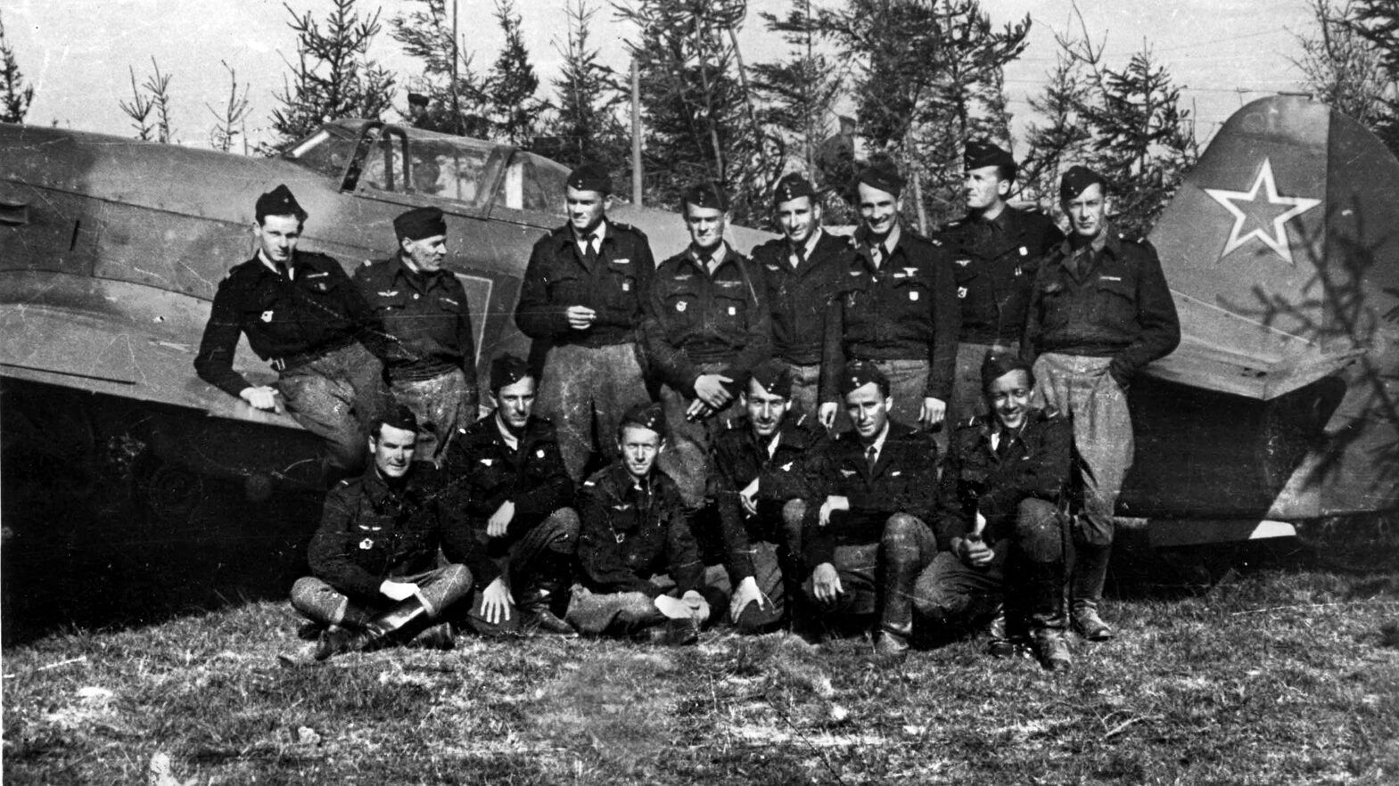Roger Sauvage sits at far right in this photograph of Free French pilots belonging to the Normandie Niemen squadron. A Yak fighter plane serves as the backdrop for the image.