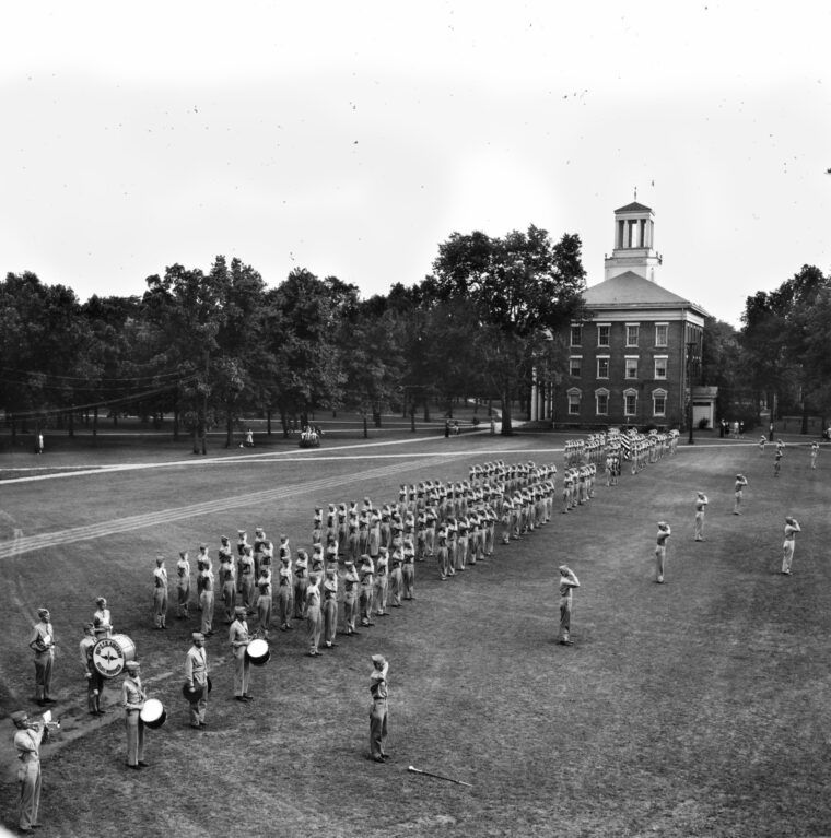 Aviation cadets, 150 strong, salute the flag during Retreat on the parade ground at Beloit College. The school’s first building, known as Middle College, is in the background.