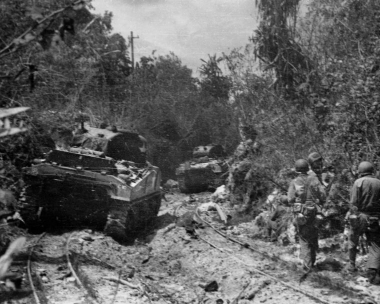 Soldiers of the 322nd Infantry Regiment, accompanied by Sherman tanks of the 710th Tank Battalion, follow narrow-gauge railroad tracks that lead to Angaur’s phosphate plant and Lake Salome.