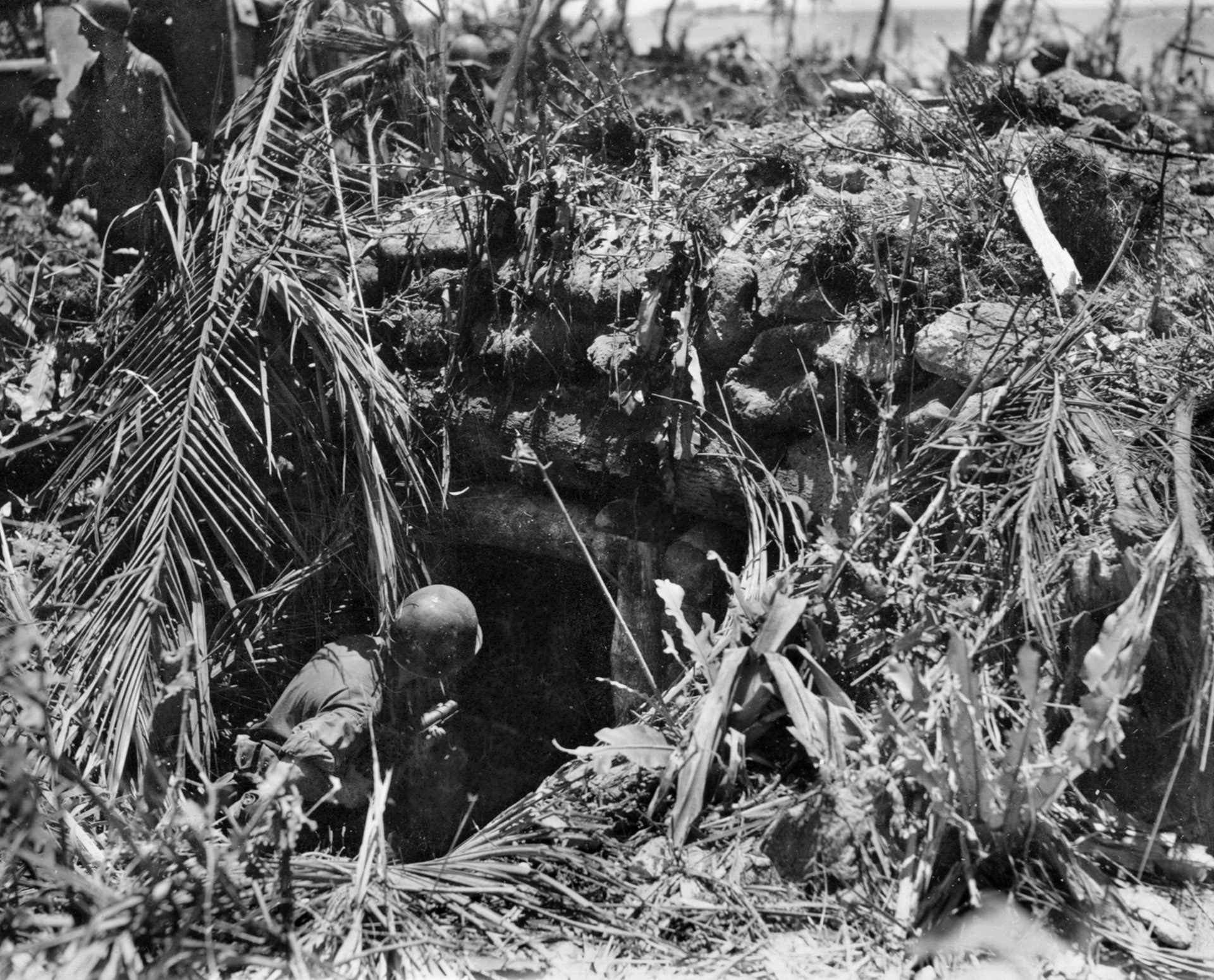 An American soldier, his weapon at the ready, cautiously inspects a well-camouflaged Japanese pillbox.