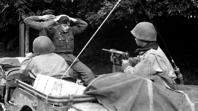 The American soldier at right covers two Germans captured north of Lorient France in August 1944 with his M-3 submachine gun.