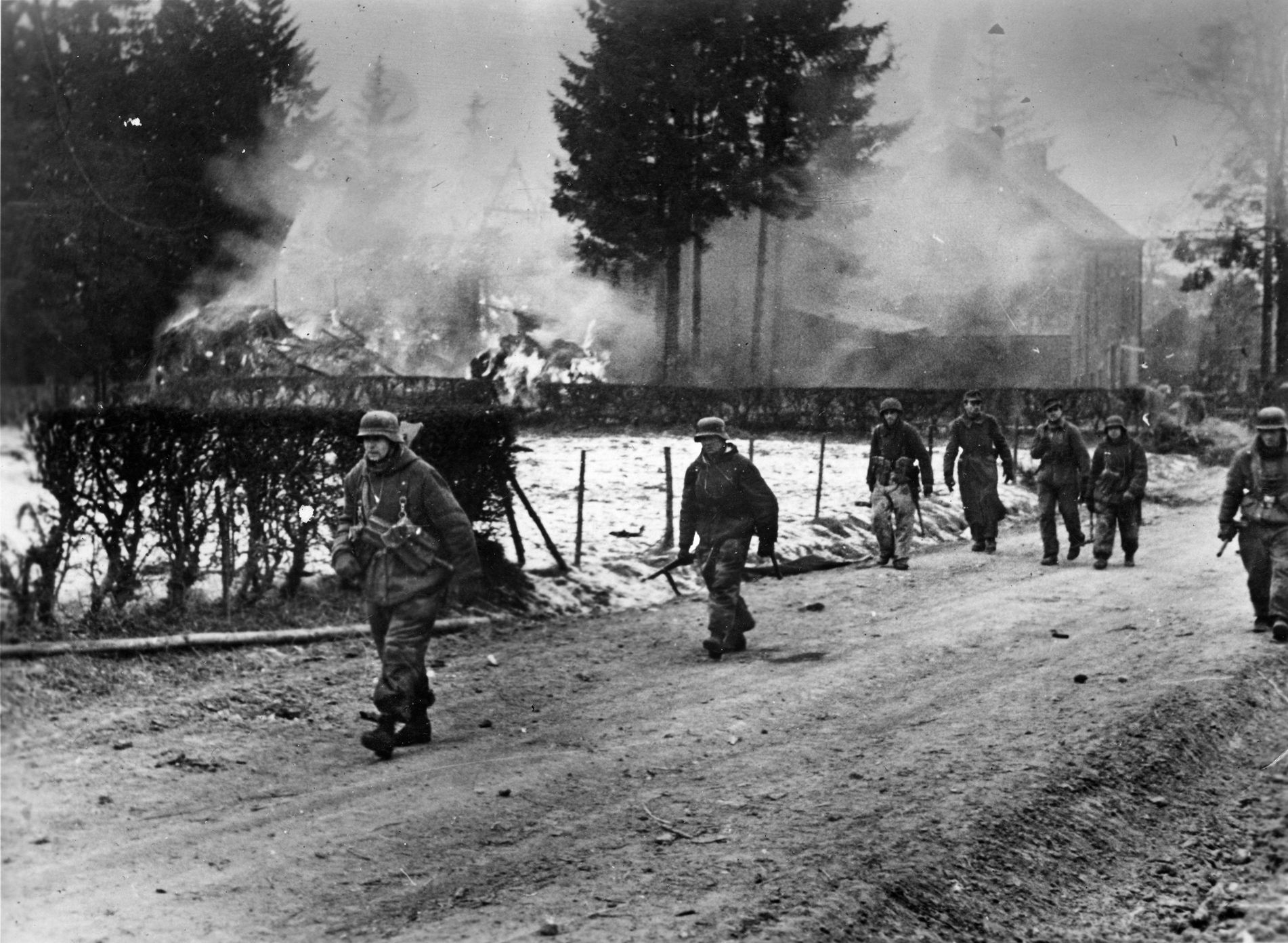 Photographed on the move prior to Operation Veritable, German panzergrenadiers move through a village as several buildings are consumed by flames. Battle-hardened German soldiers mounted effective defensive efforts in the Reichswald, delaying the movement of British forces deeper into the industrialized Ruhr.