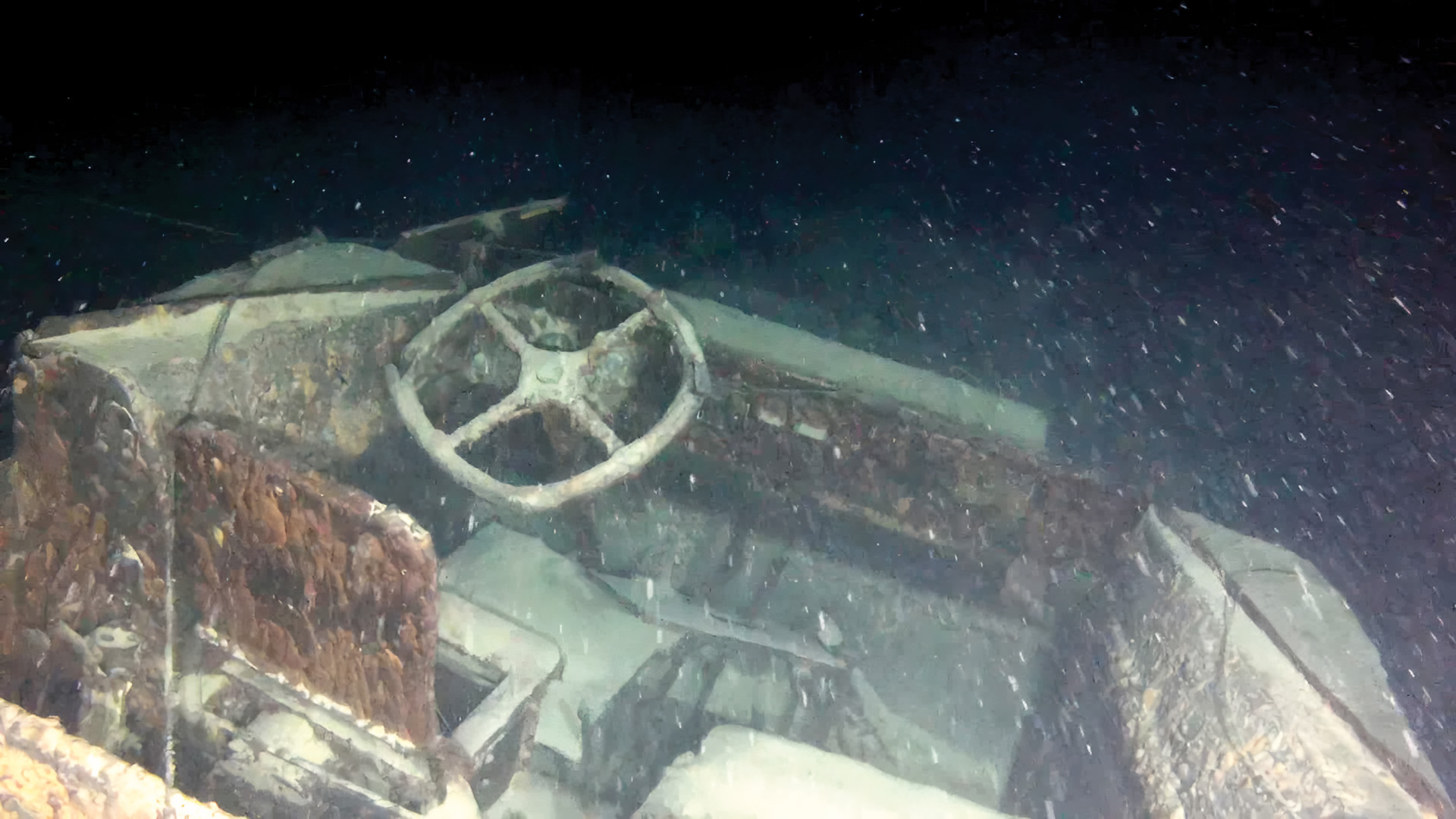 A picture taken by the ROV of the driver’s position on the DUKW. The instrument gauges are still visible although a portion of the dashboard has fallen off. The rubber-coated steering wheel is still largely intact.