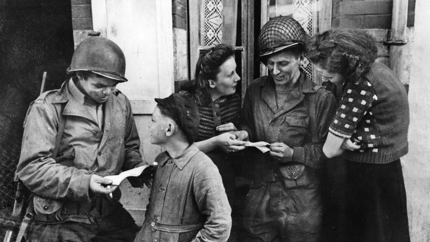 In Isigny, two French women and a boy help American soldiers read French.