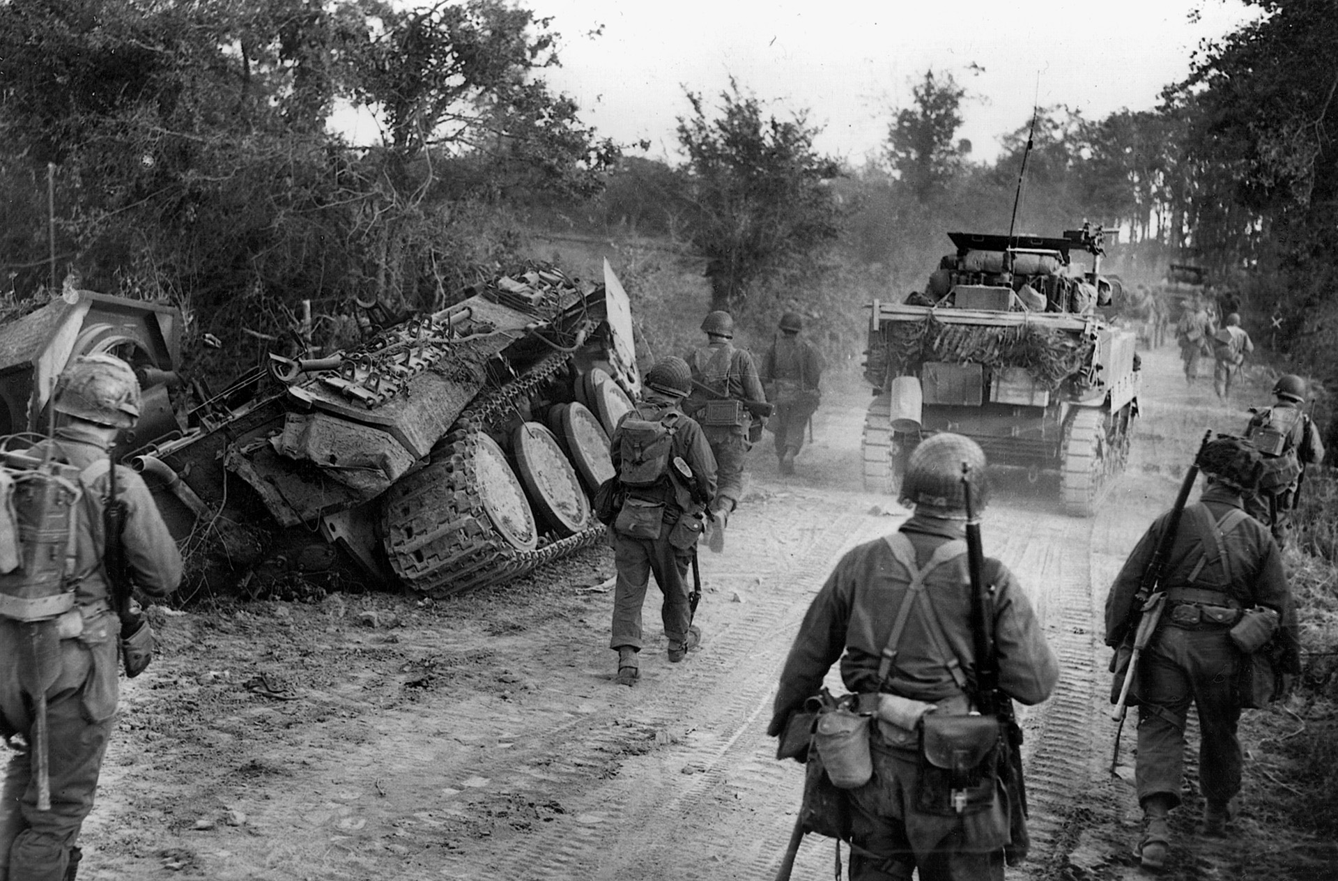 American footsoldiers and armor pass a destroyed panzer. Cobra was marked by lightning advances that made George Patton and Third Army household names in America.