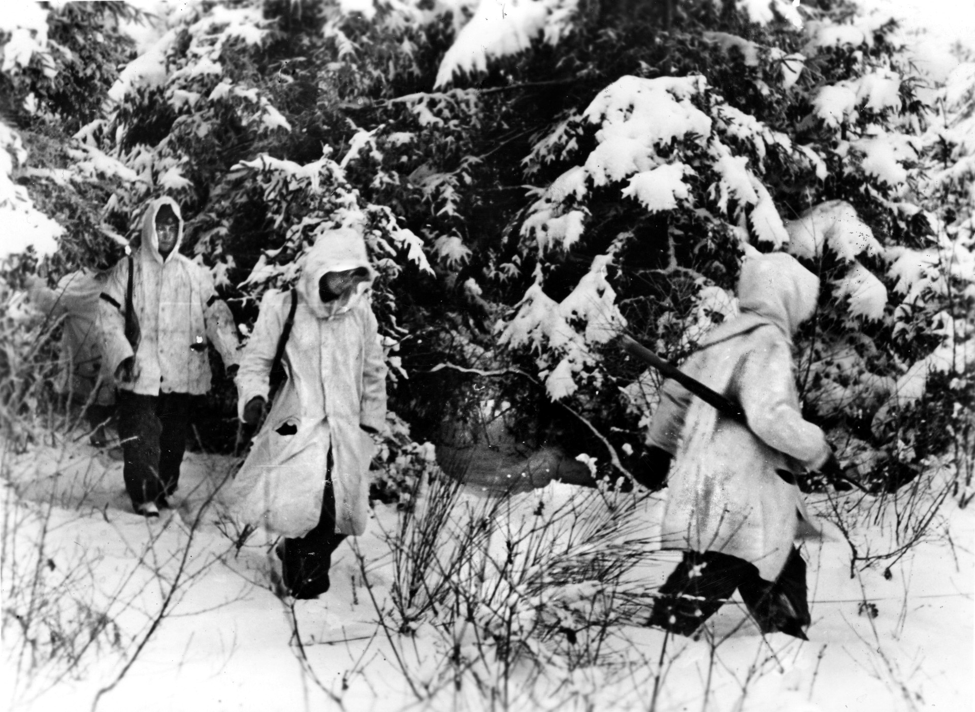 A German scouting party, dressed in white camouflage smocks, moves through a snowy forest. Clifford Savage, 99th Infantry Division, recalled seeing Germans wearing “white bedsheets” during the attack.