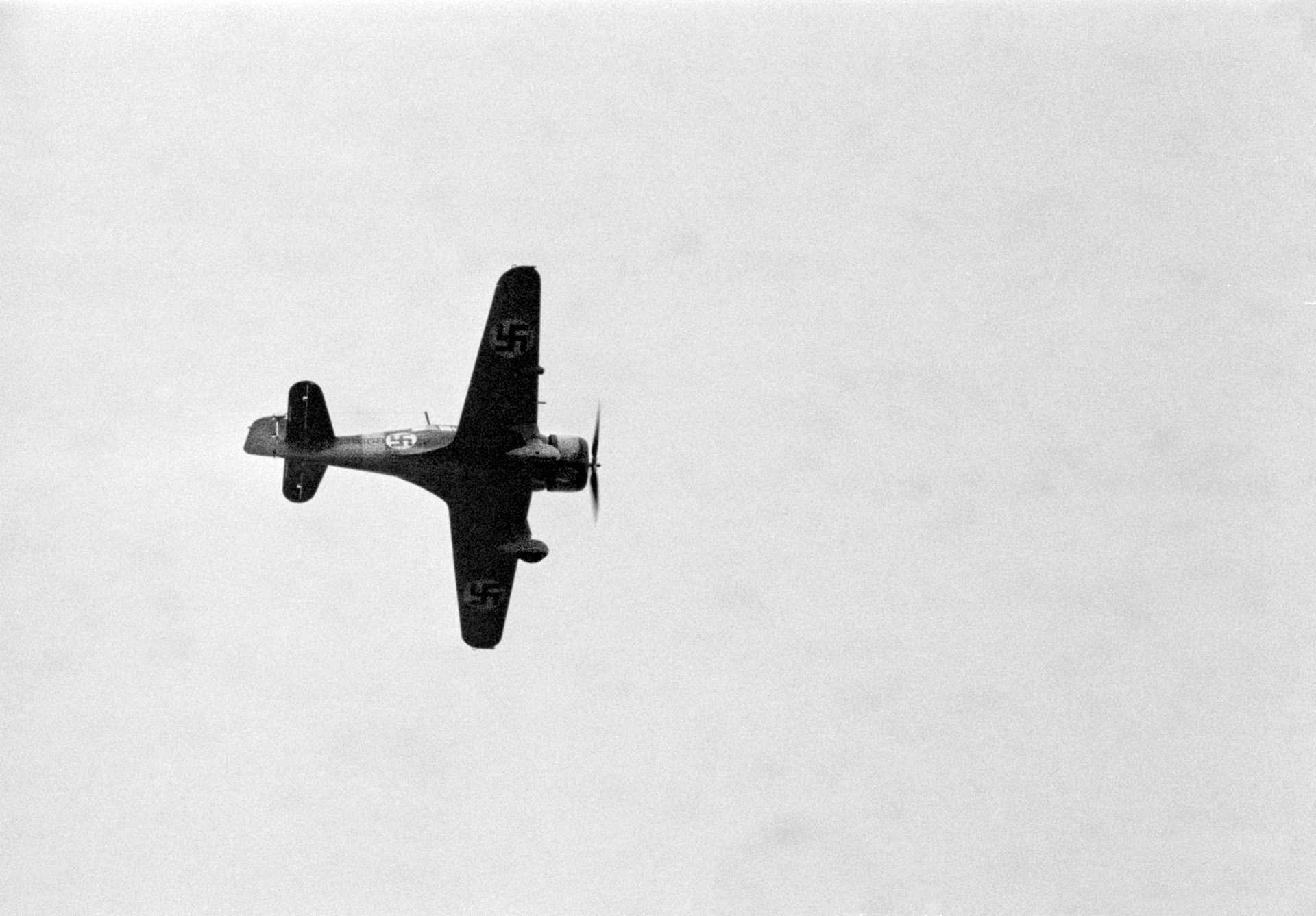 A Fokker D.XXI of the Finnish Air Force with a blue swastika painted on the fuselage flies overhead. The symbol had nothing to do with Nazi Germany, and dates to 1918.