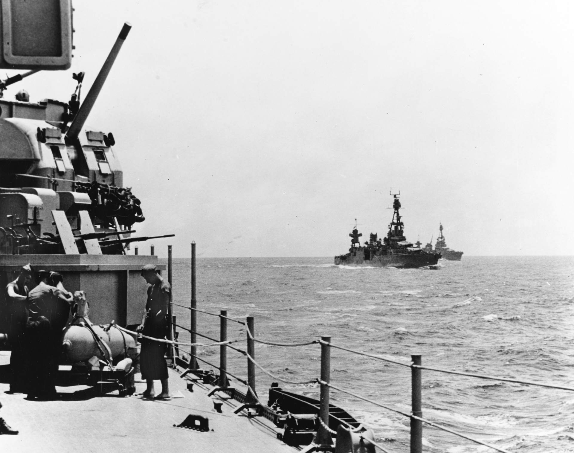 Sailors aboard the cruiser USS Wichita work to make ready a paravane, an anti-mine device, as other cruisers of Task Force 18 sail toward Rennell Island. The USS Chicago, center right, was sunk by Japanese warplanes on January 30, 1943, the day after this photo was taken. 