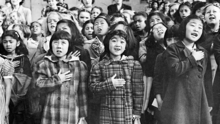 Japanese American children at the Raphael Weill Public School in San Francisco recite the Pledge of Allegiance, April 1942. The two girls in the front row were both sent to internment camps along with their parents.