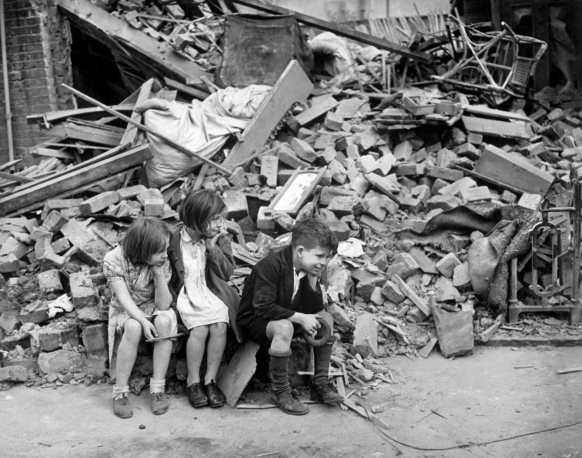 Children of East London who were made homeless during the raids in September 1940 glumly sit in the rubble of their home.