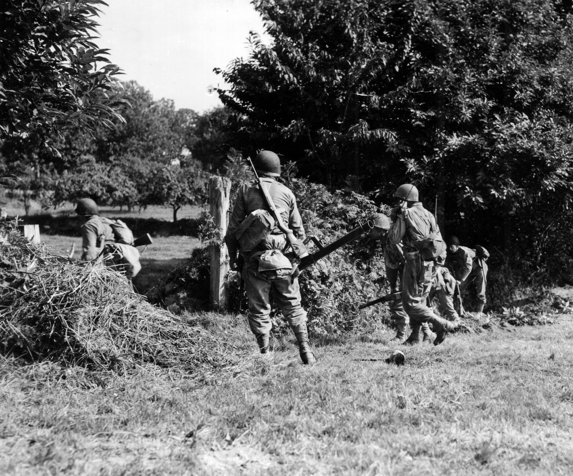 Men from Company A, 11th Infantry, 30th Division, advance through a break in the hedgerows on August 9. The soldier at right is using his handy-talky radio.