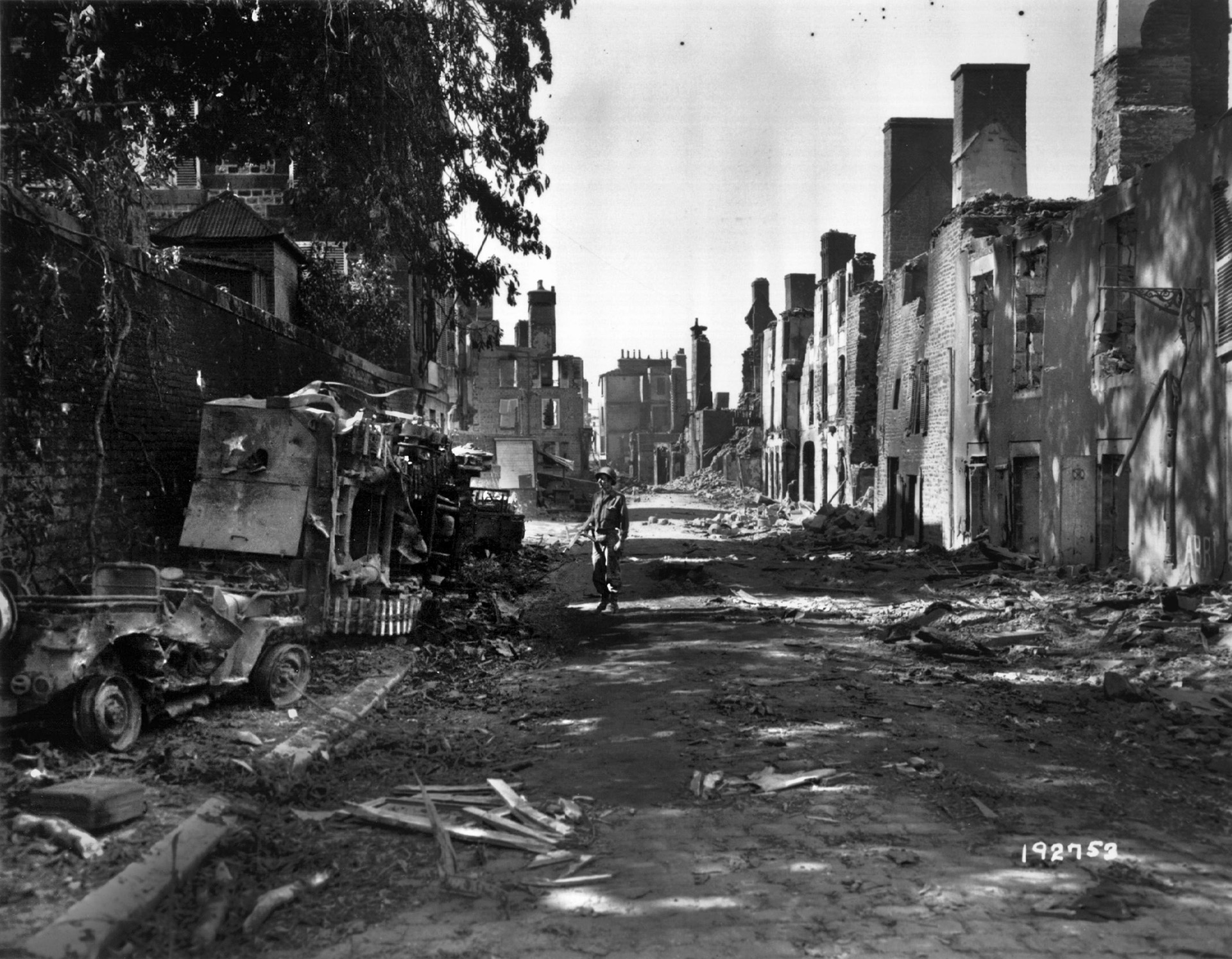 A GI on the La Grande Rue, Mortain's main street, looks at destroyed American vehicles, August 12, 1944.