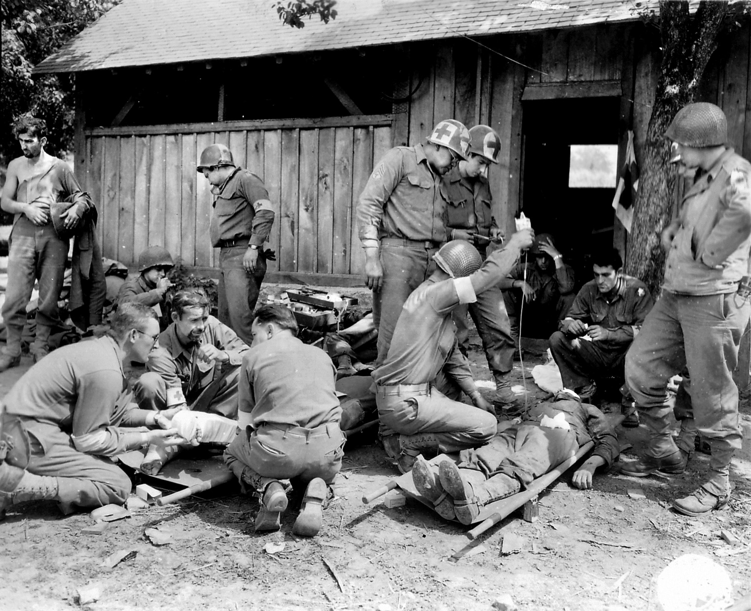 A leg splint is placed on a soldier (left) at a forward medical aid station set up near Mortain on August 12 while plasma is given to a soldier at right who suffered a head wound. 