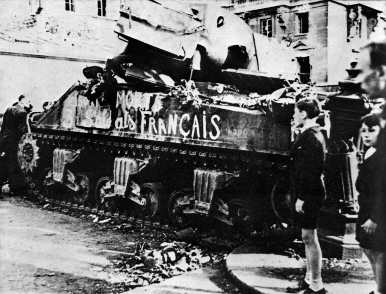 A French Sherman lies in ruins after being hit by anti-tank fire. The painted inscription on the side says that its three crewmen died for France.