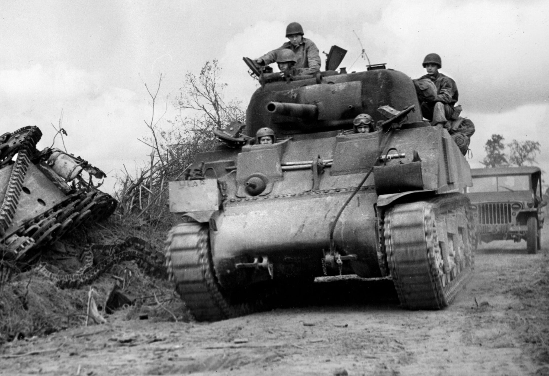 An American Sherman tank sweeps past an upended panzer on a country lane in Normandy. German armored forces suffered huge losses during Cobra.