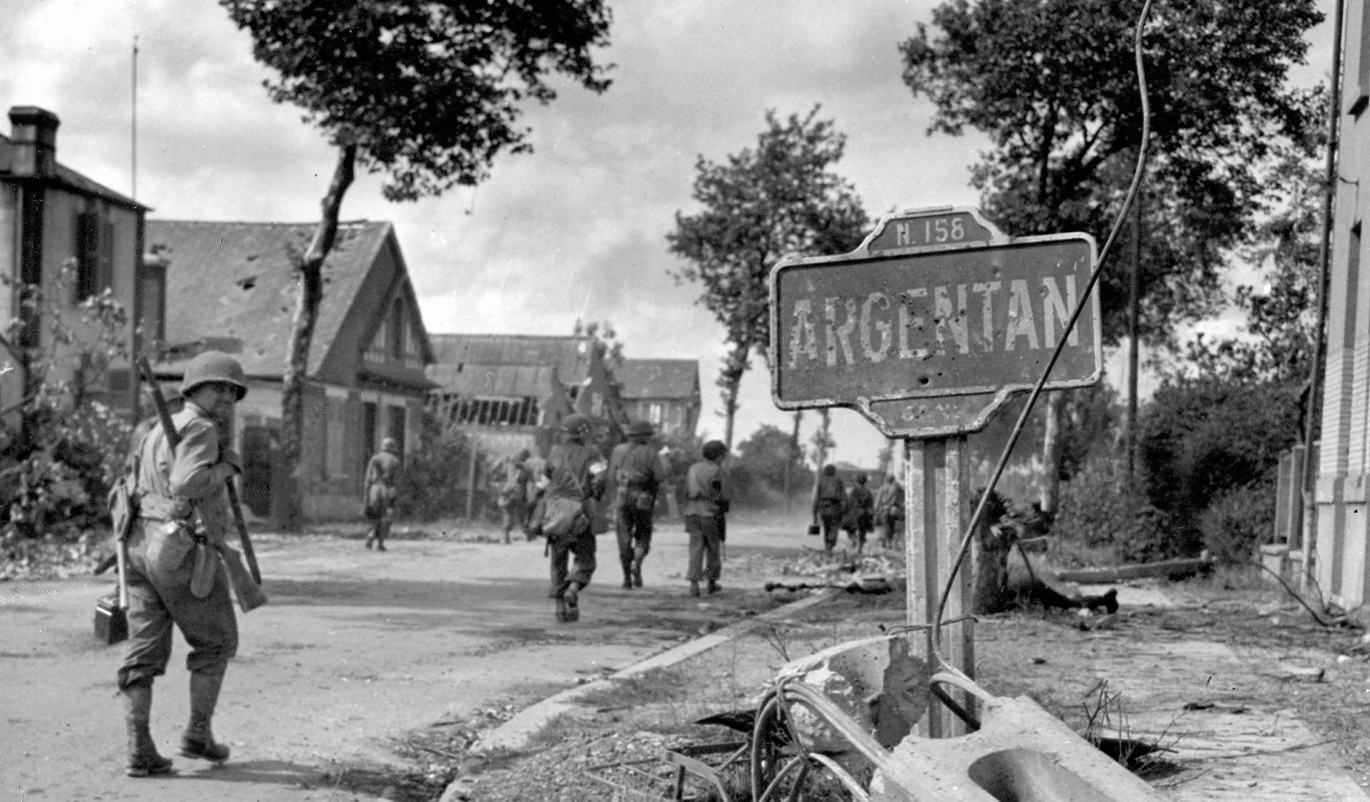 An American rifleman glances back at the photographer as his unit enters the shot-up town of Argentan, August 20, 1944.