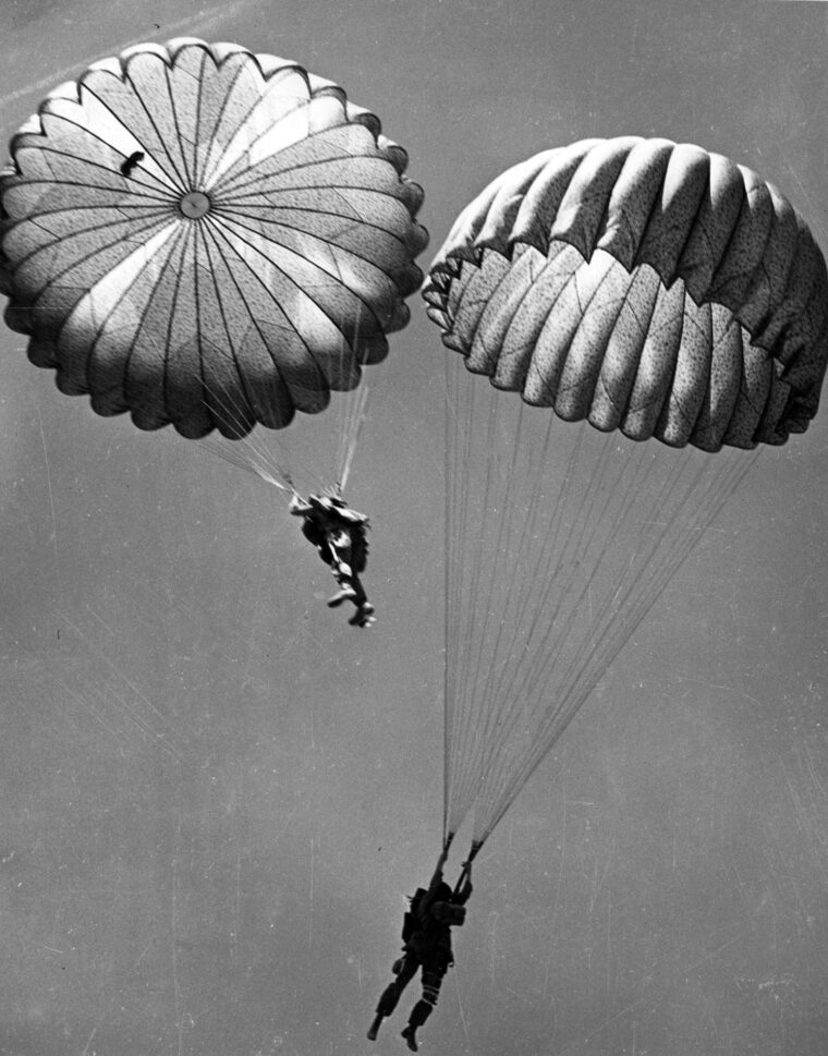 Their parachutes billowing above them, American paratroopers are shown descending earthward during a parachute jump in North Africa.