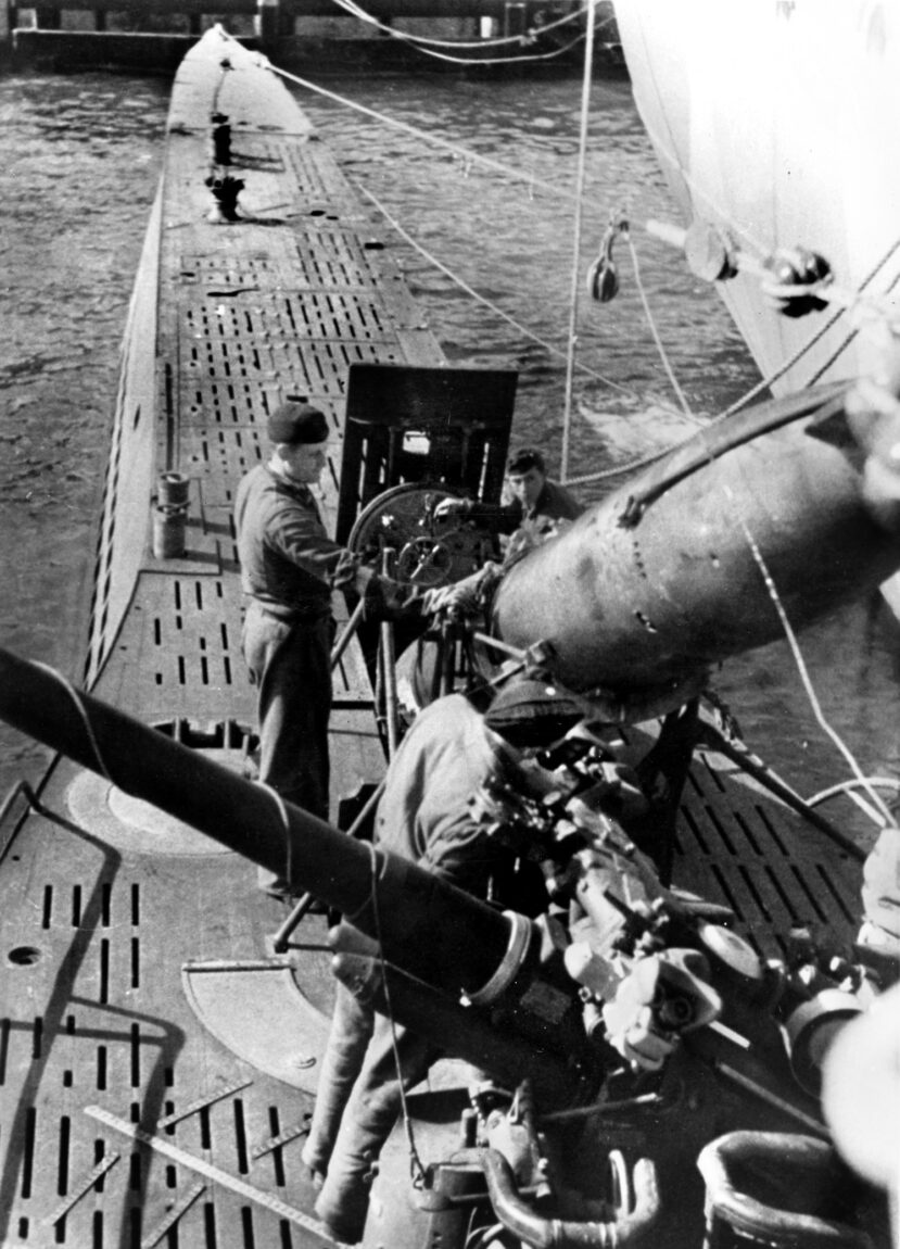 German submarine crewmen load torpedoes aboard the Type-VII submarine at a port in occupied Norway prior to departure for a war patrol. The barrel of the U-boat’s 88mm deck gun is visible. 