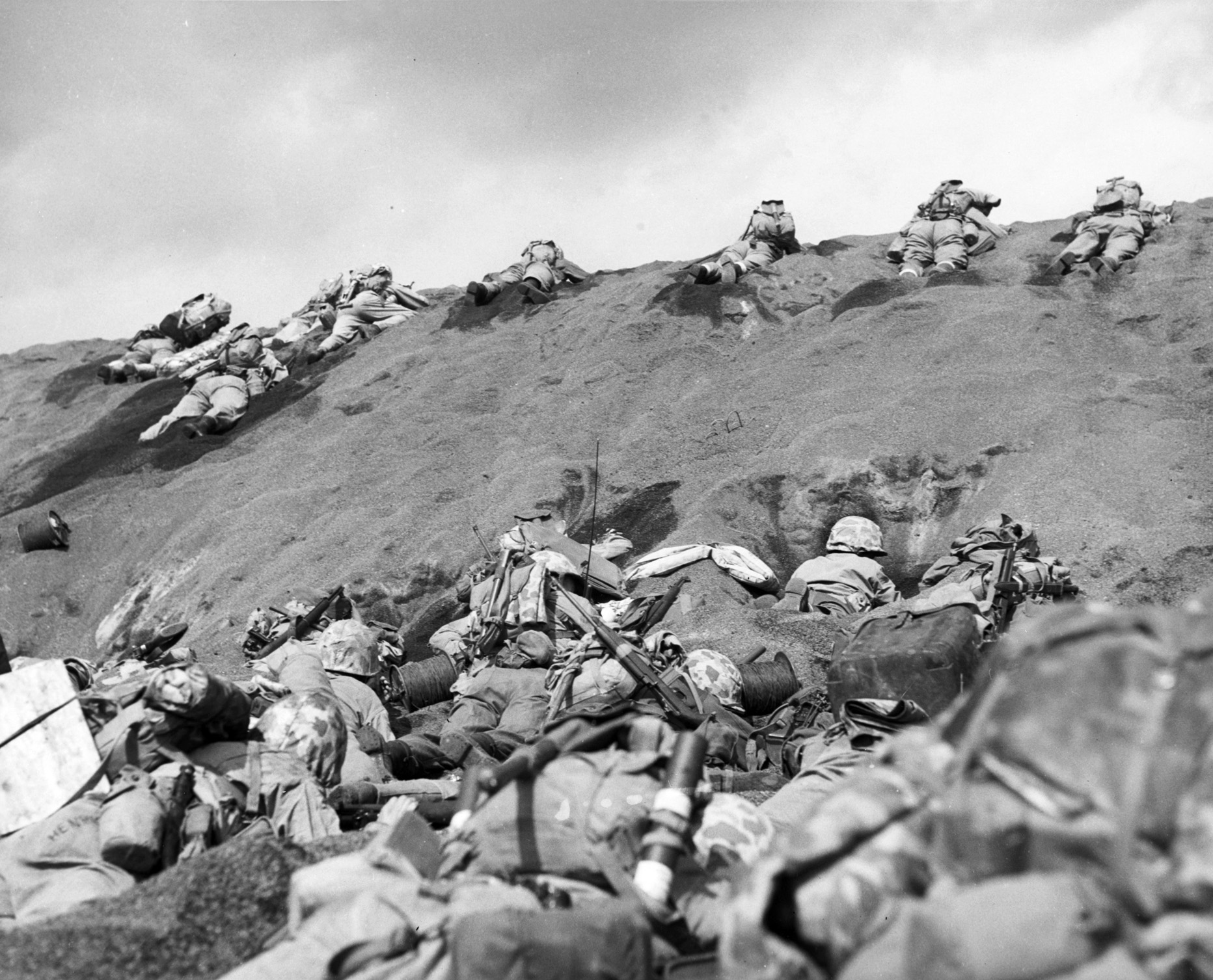 During the initial landings on Iwo Jima on February 19, 1945, U.S. Marines of the Fifth Division take heavy Japanese fire as they struggle up a slope off Red Beach 1. The black volcanic sand of Iwo Jima was difficult for Marines to traverse, and tracked and wheeled vehicles often bogged down.