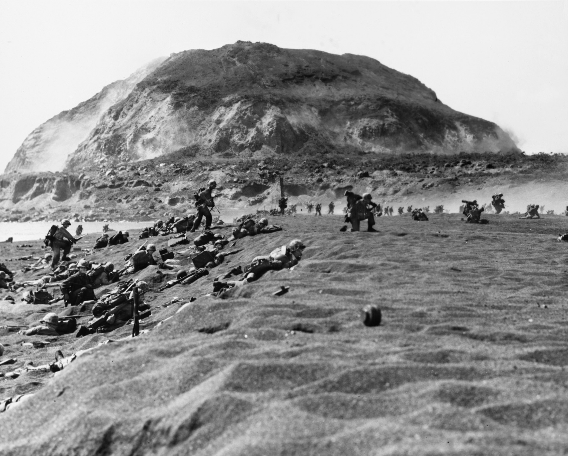 With the heights of Mount Suribachi looming in the distance, Marines of the Fifth Division move inland from the invasion beaches at Iwo Jima after landing on February 19, 1945.