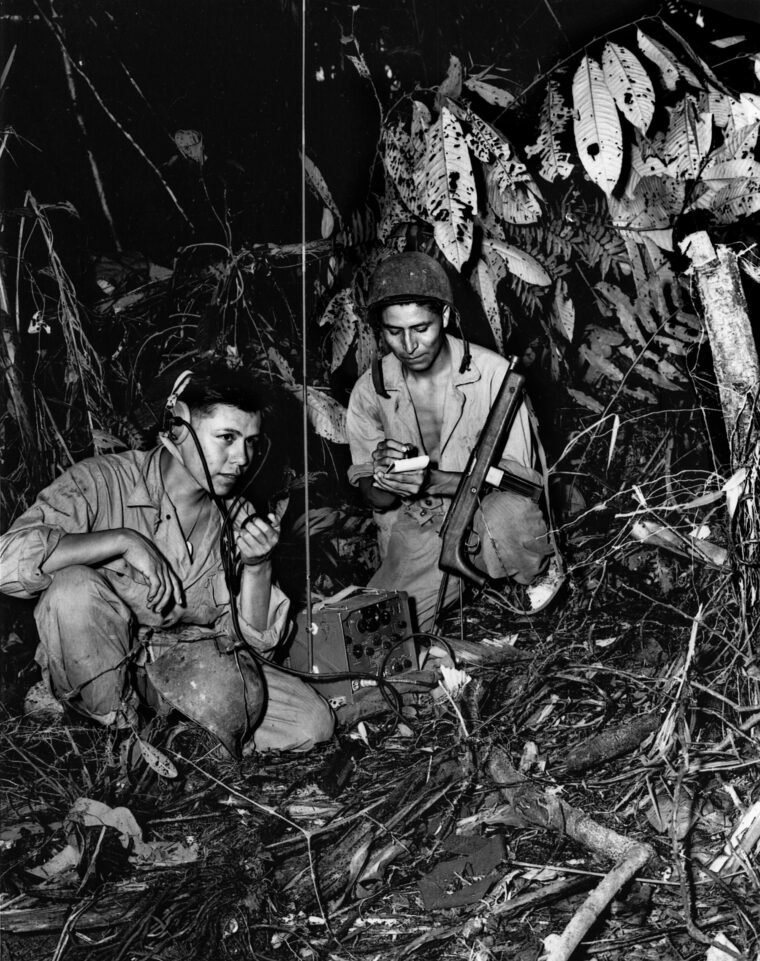 While operating on  Bougainville in December 1943, Navajo code talkers Corporal Henry Bake, Jr., (left) and Pfc. George H. Kirk establish communications by radio from a clearing in the jungle they have hacked out with machetes. 