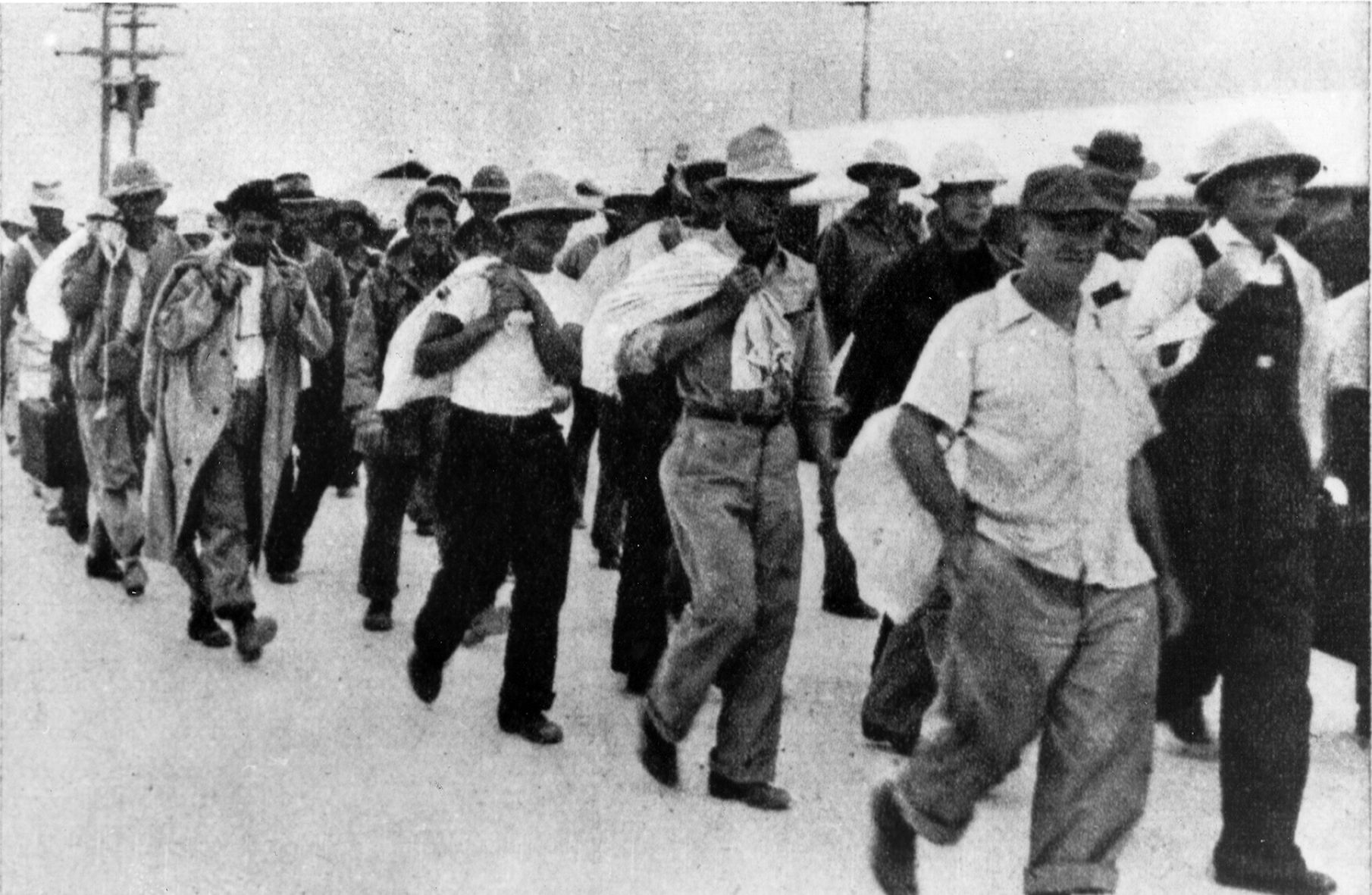 Prisoners of the Japanese, U.S. military and civilian personnel are marched to the waiting transport ship Nita Maru on Wake Island on January 12, 1942. Several of the prisoners are wearing sun helmets similar to the one brought home by Glen Binge.