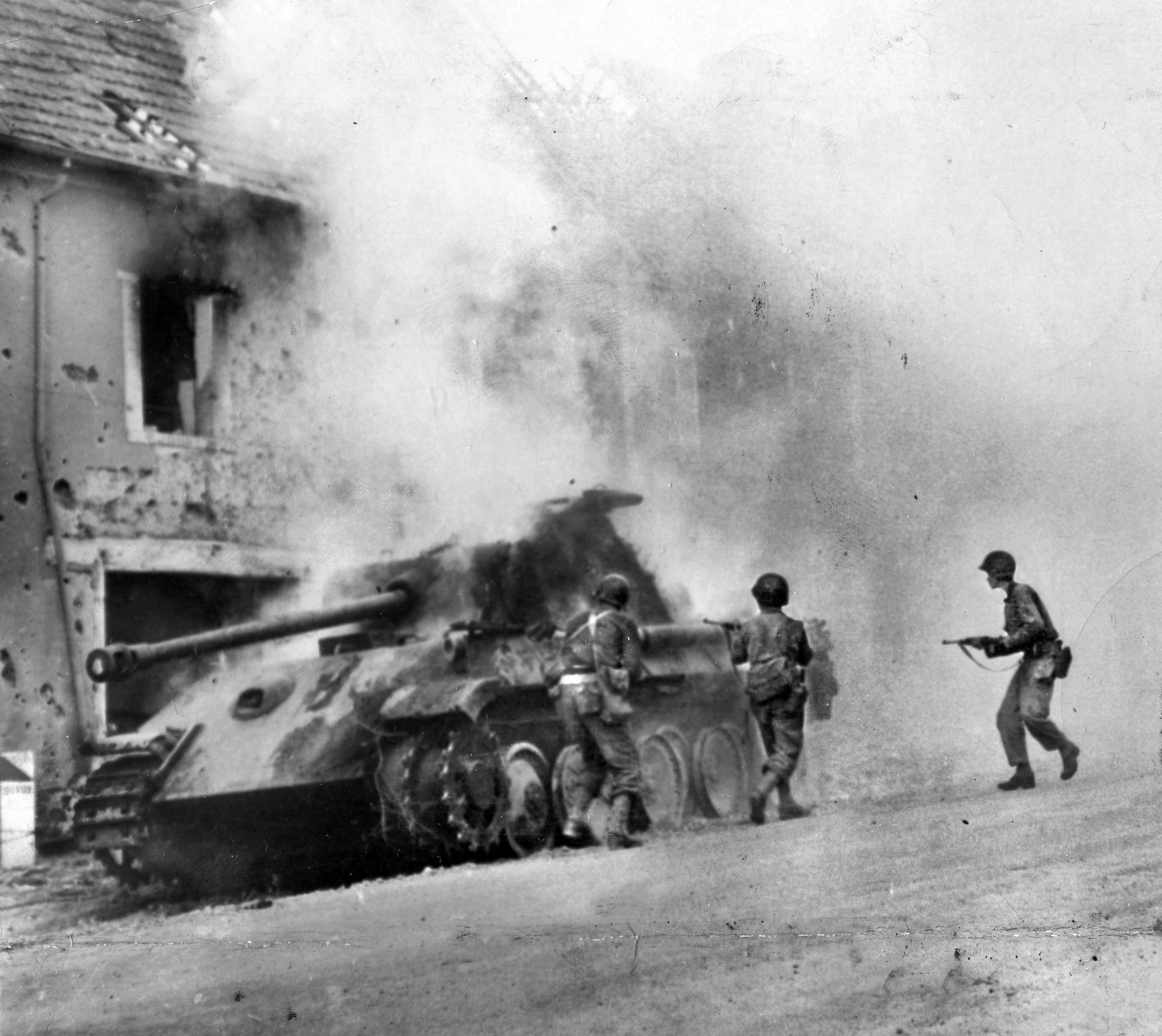 American infantrymen cautiously approach a burning German Tiger I that they have just knocked out of action in the fighting around Mortain. After the battle, the surviving German forces retreated towards Falaise where many would meet destruction.