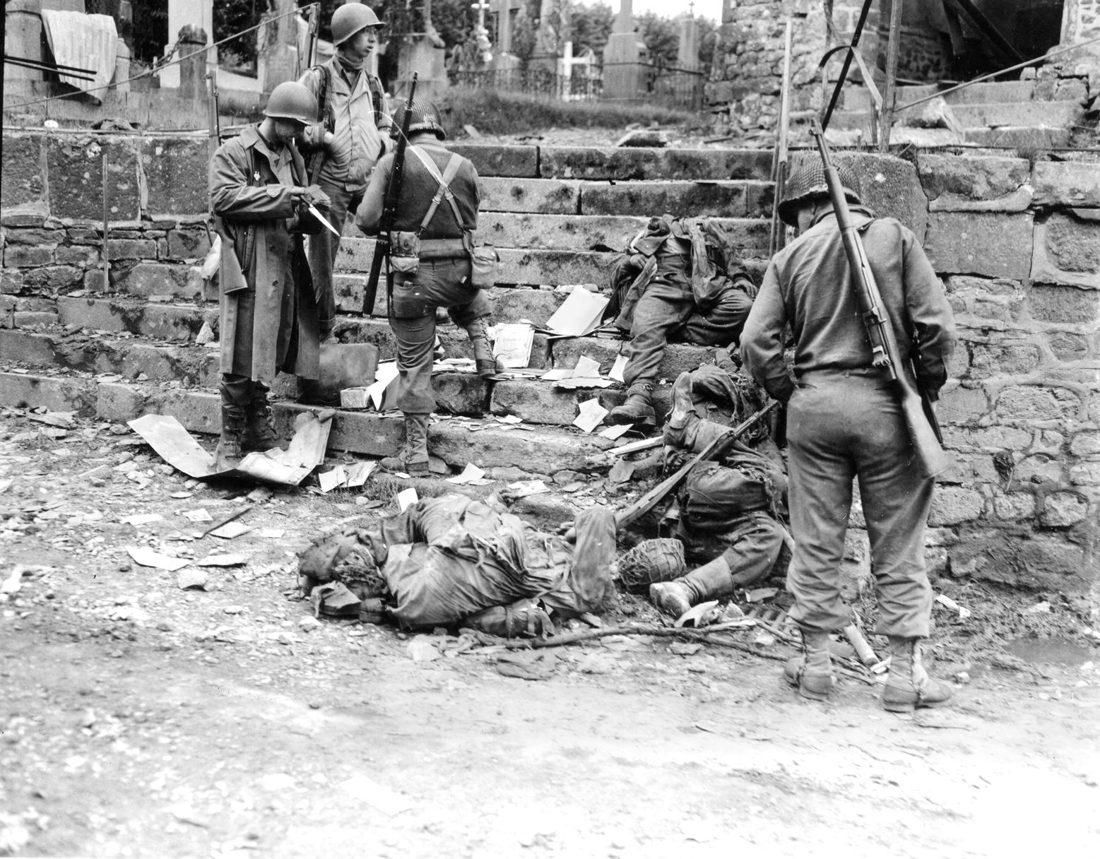 U.S. infantrymen examine the possessions of German casualties in the town of Notre Dame de Cenilly at the beginning of Operation Cobra.