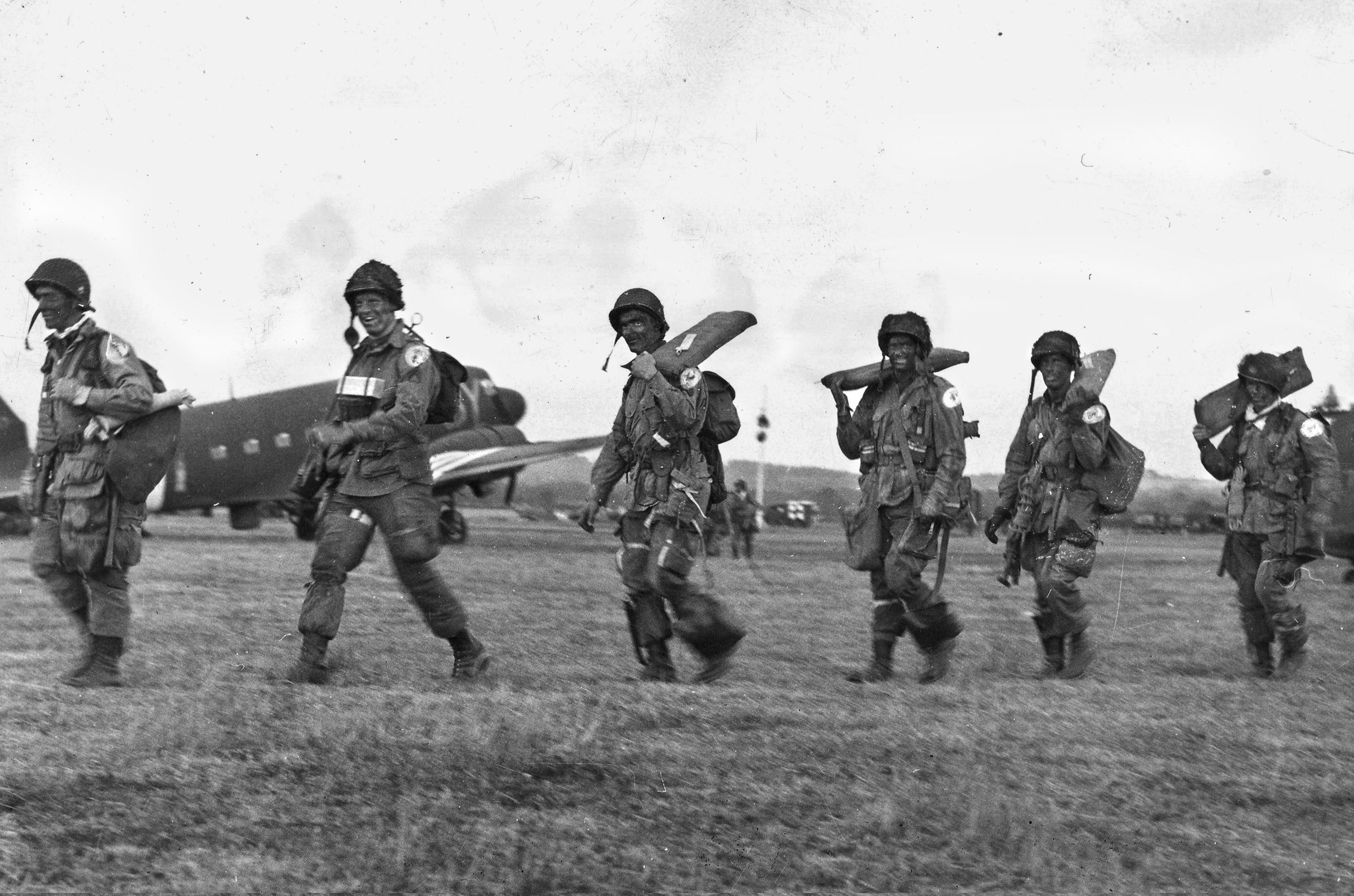 With faces blackened and their divisional insignia obscured by a censor’s brush, these smiling, heavily laden paratroopers prepare to board their transport plane, June 5, 1944. 