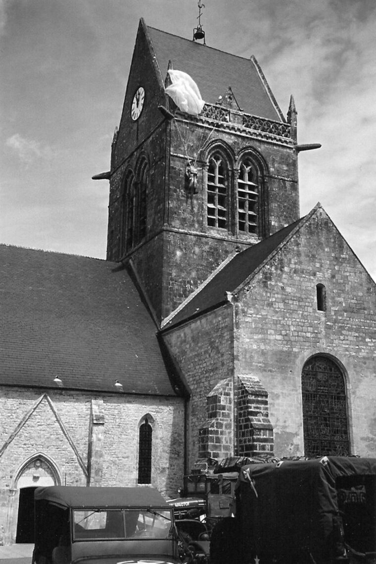 A dummy representing Private John Steele, F Company, 505th PIR, 82nd Airborne Division, still hangs from the steeple of the church in Sainte-Mère-Église. In actuality, Steele hung from the opposite side of the steeple.  
