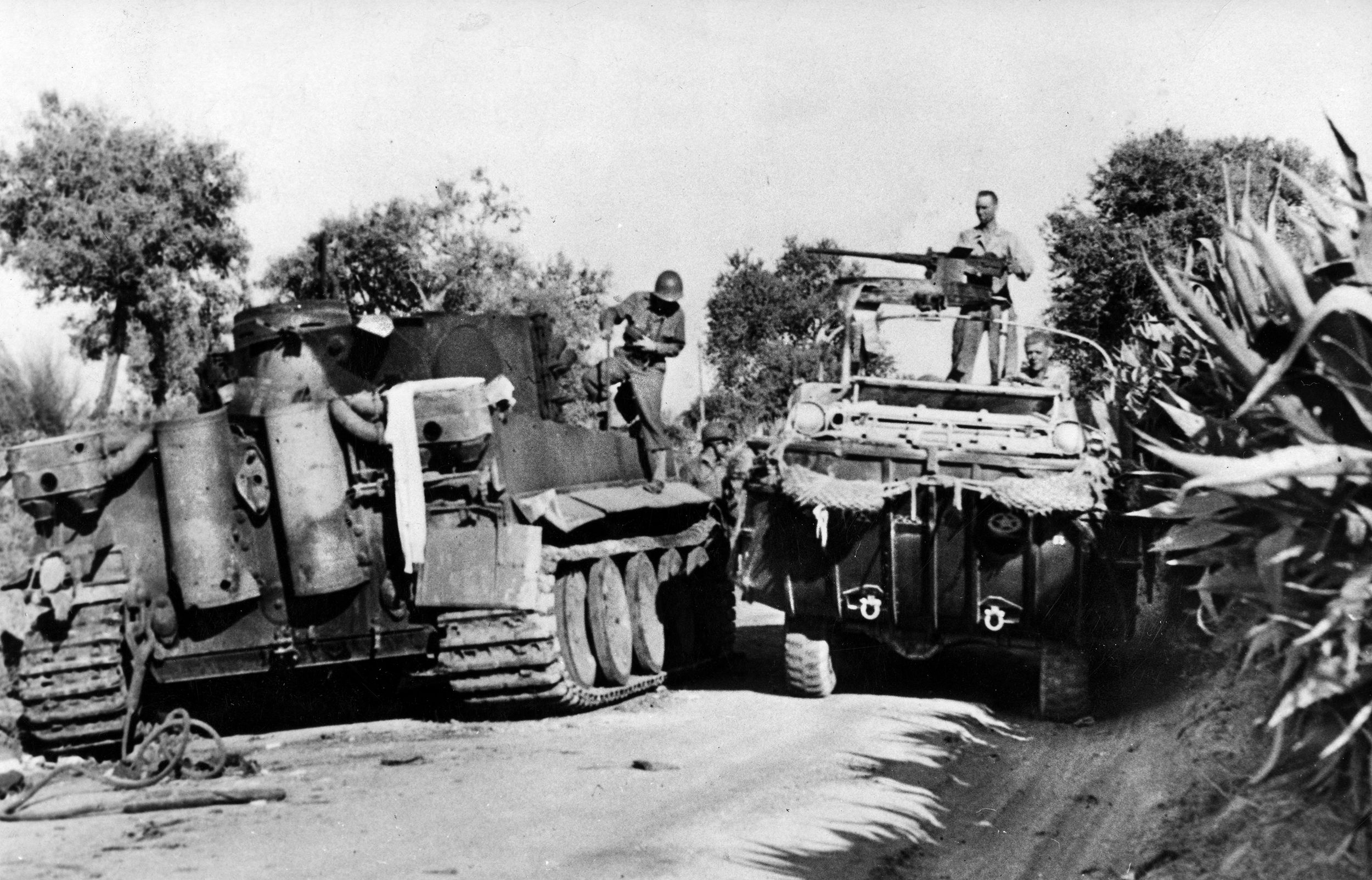 An amphibious GMC DUKW (“Duck”), mounting a .50 caliber machine gun, squeezes past a knocked-out German Mark VI Tiger tank from the Hermann Göring Panzer Division. The enemy division first tried to stop the Allied invasion but then fought a delaying action so that German and Italian troops could escape from Messina to the mainland of Italy.