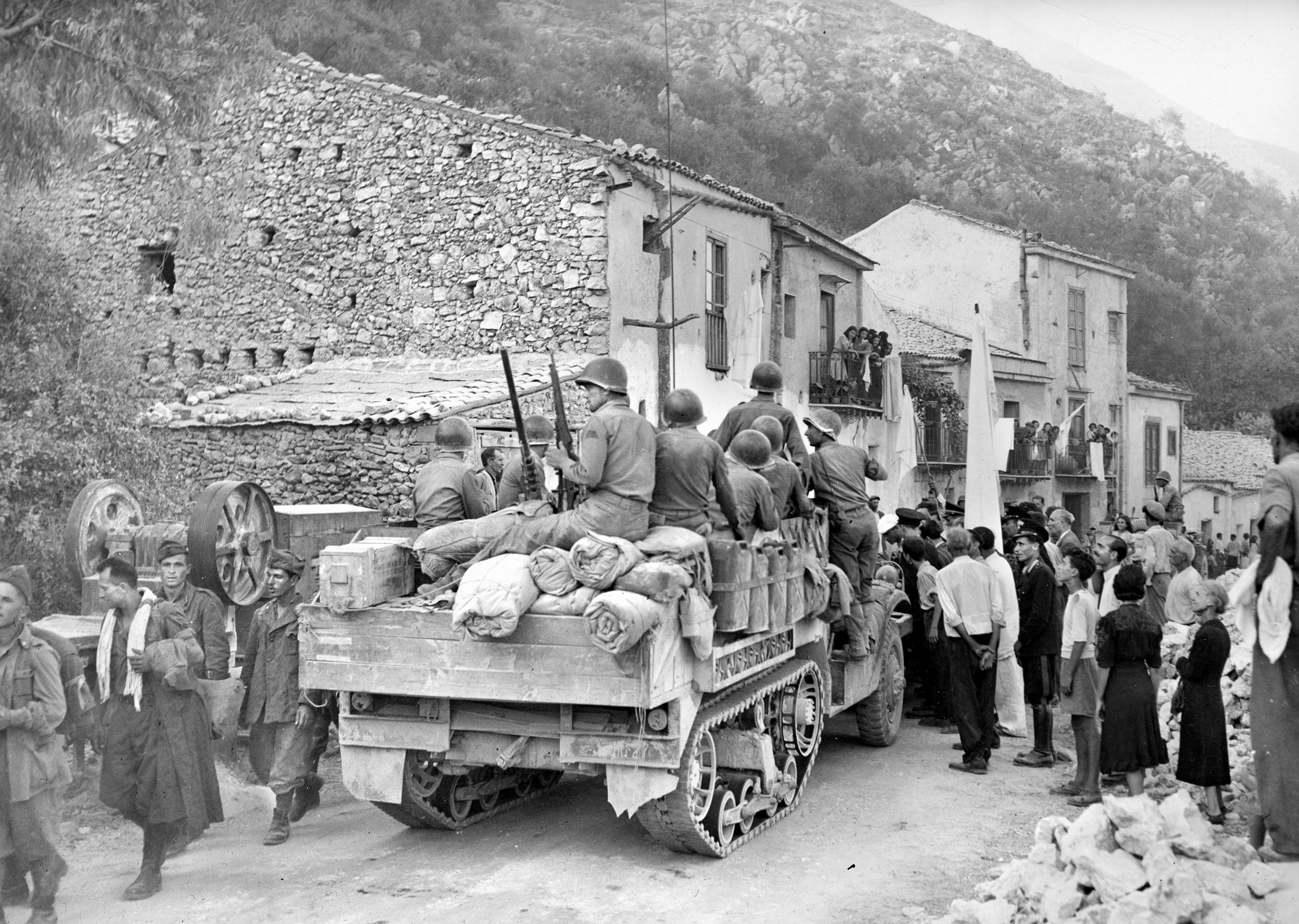 American soldiers on an M3 halftrack are greeted by civilians in the liberated Palermo suburb of Pioppo while captured Italian soldiers (left) are marched to the rear.