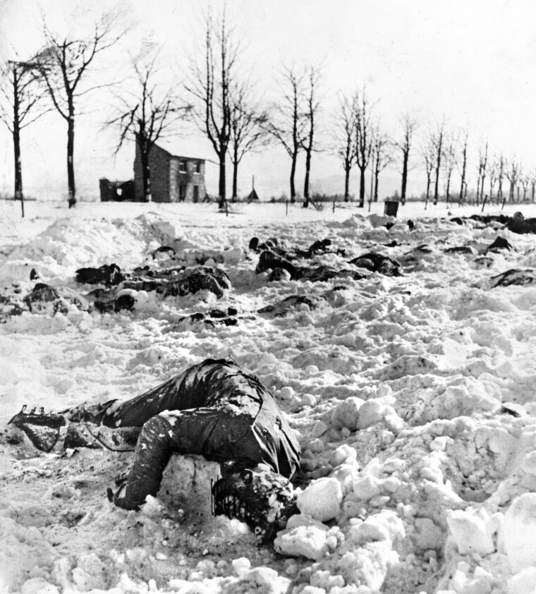 The frozen bodies of U.S. solders lie in a snowy field at Baugnez, near Malmédy. An Army censor has obscured the face of the nearest casualty. Madame Bodarwe’s burned tavern is in the background.