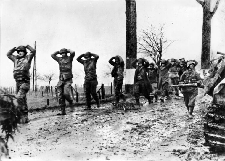 German troops march a line of Americans to the rear, where they will be packed into railroad boxcars and transported to POW camps deep inside Germany.