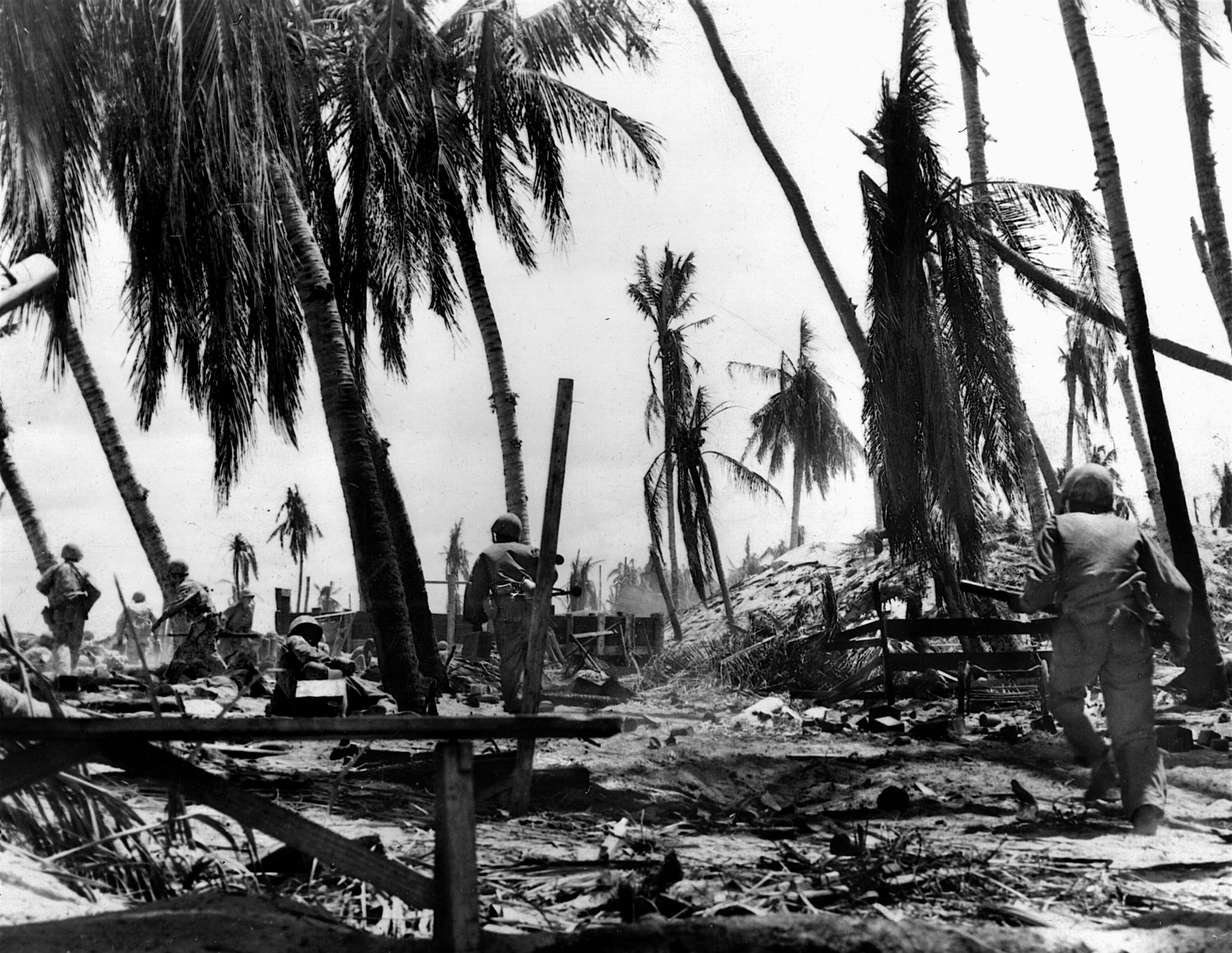 Advancing through a forest of blasted palm trees, Marines head for a sand-covered Japanese bunker. Fewer than 200 defenders, most of them non-combat Korean laborers, survived the onslaught.