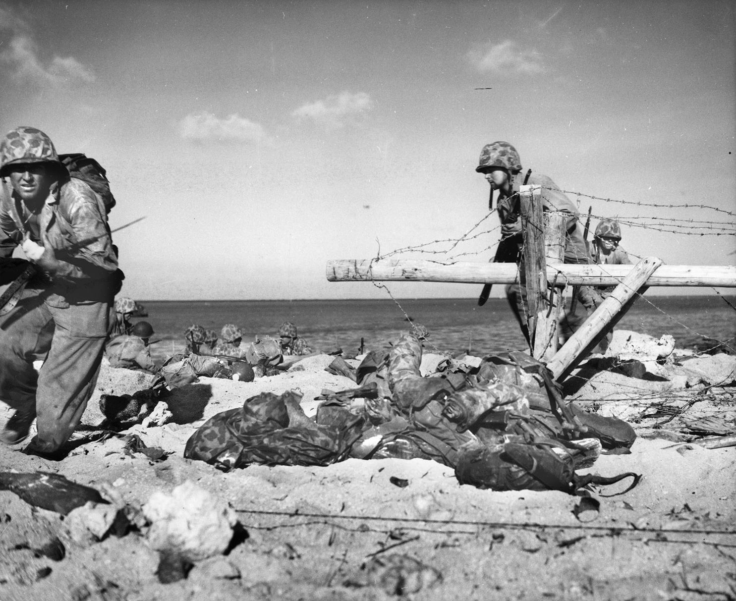 Marine with fixed bayonet and a bandage on his wounded hand, left, leads others around a barbed wire entanglement on the beach at Tarawa.