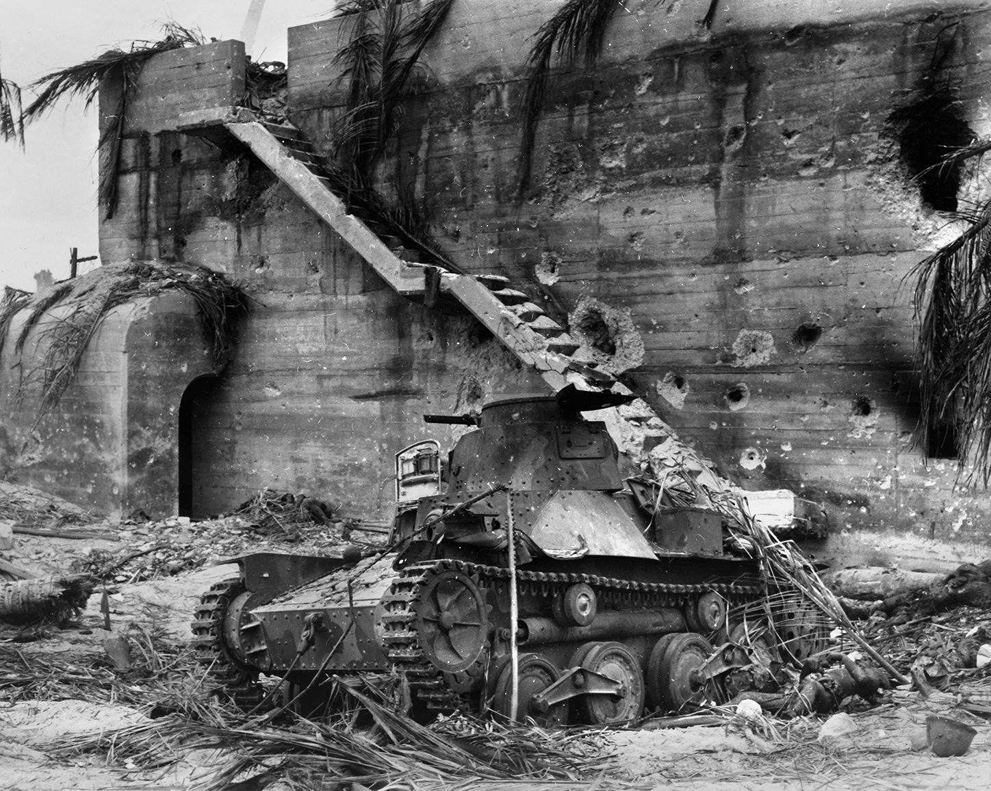 The effects of naval shelling are clearly visible on the rear concrete wall of Rear Adm. Keiji Shibasaki's command bunker. A dead Japanese soldier lies beside a knocked-out Type 95 Ha-Go light tank. 