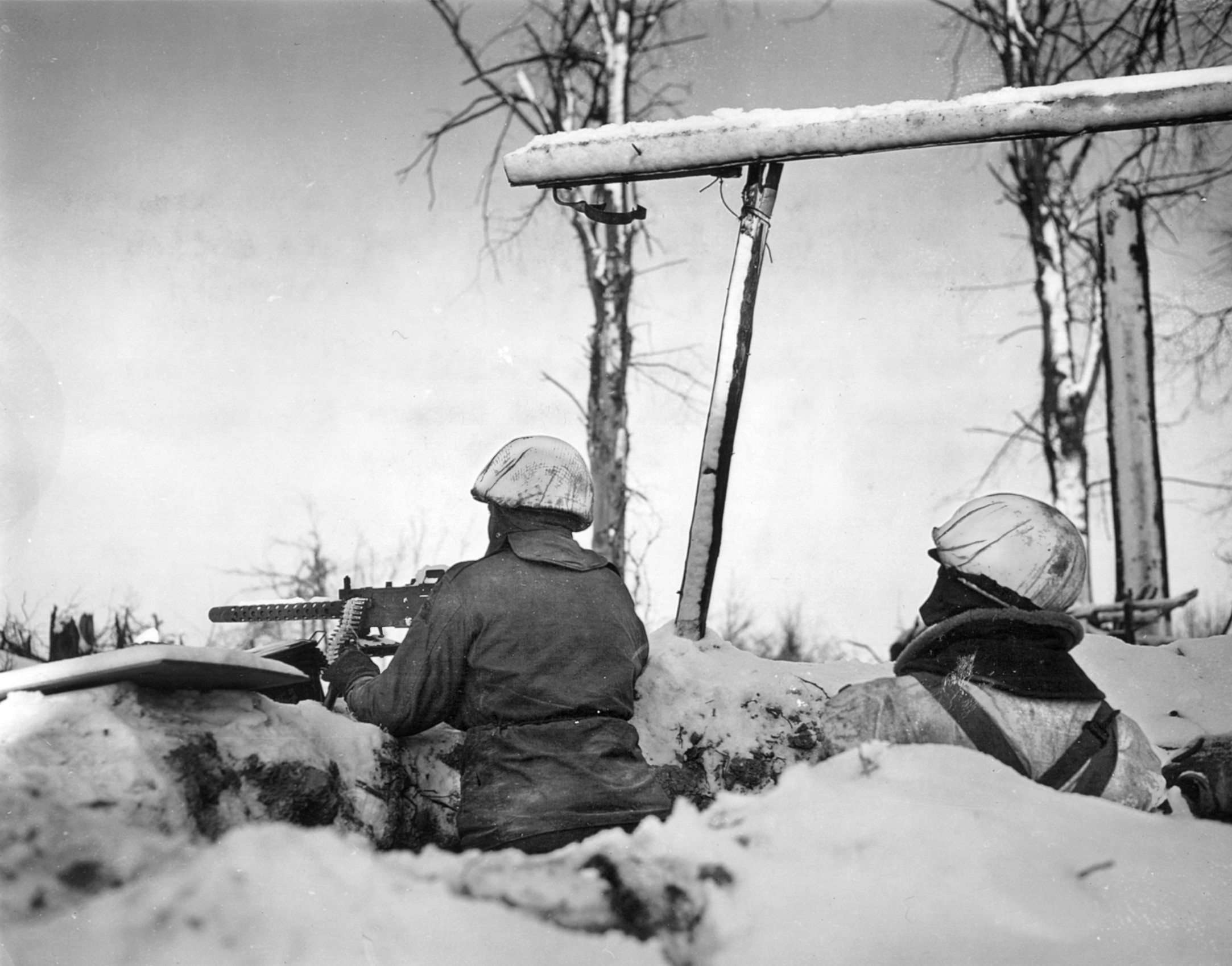 Camouflaged to blend into the winter landscape, two soldiers of the 7th Armored Division defend a roadblock near St. Vith.