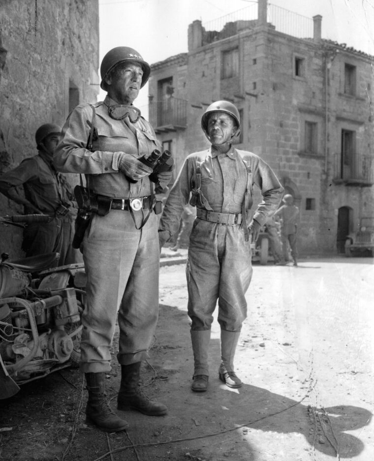 General George S. Patton Jr., and Brigadier General Ted Roosevelt stand in a street in a small town in Sicily in August 1943. Patton was in command of the U.S. Seventh Army at the time, and soon after this photo was taken, he recommended the relief of Roosevelt and General Terry Allen from command of the 1st Infantry Division.